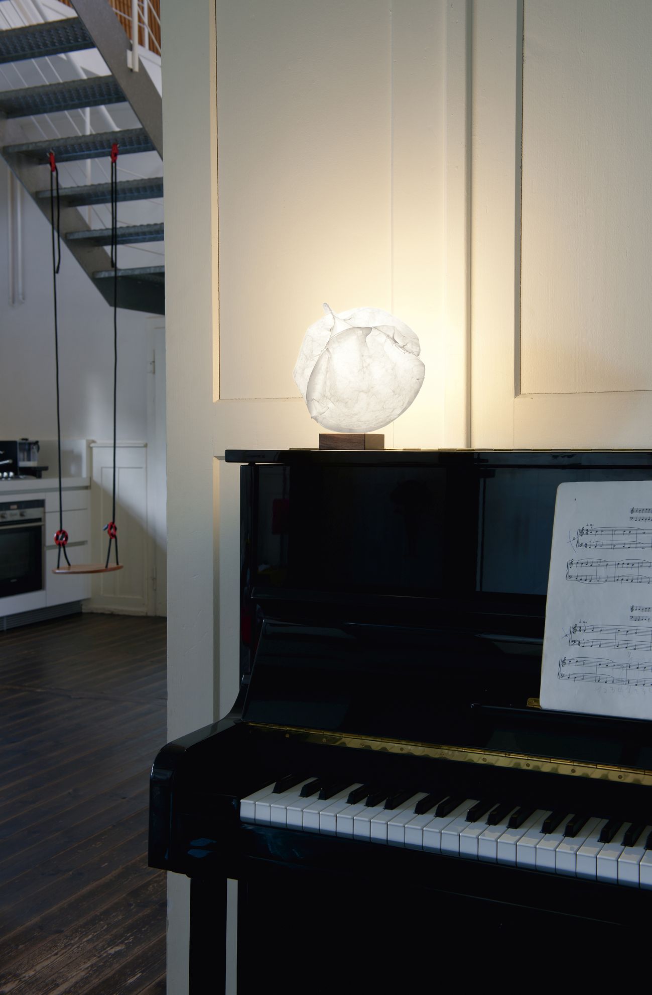 Nahaufnahme einer weißen Papier-Tischleuchte auf einem Klavier mit Notenblättern im Wohnzimmer.