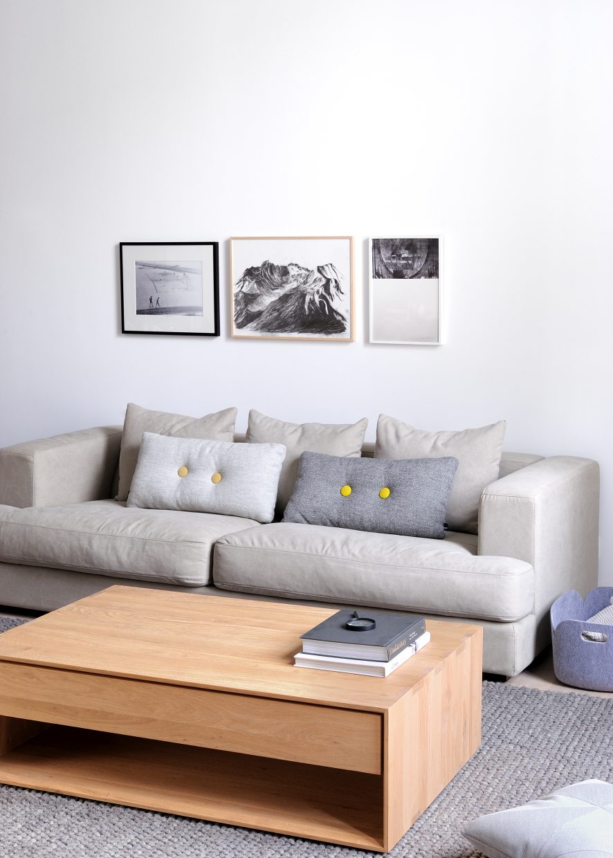 Beige Couch mit Zierkissen, Holz-Couchtisch, Teppich und Wandbildern für modernes Wohnzimmer-Interieur.