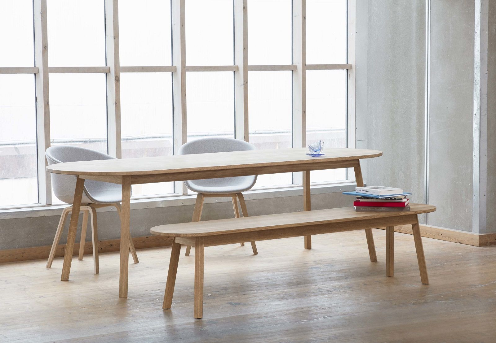 Hay Triangle Leg Table Esstisch aus Eiche mit Stühlen und Bank vor einem Fenster.