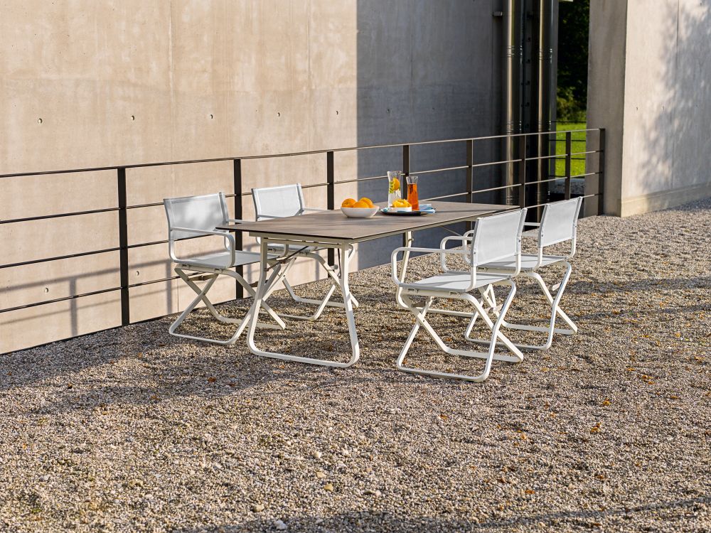 Ahoi Tisch von Weishäupl mit vier weißen Outdoor-Stühlen auf Kiesboden.