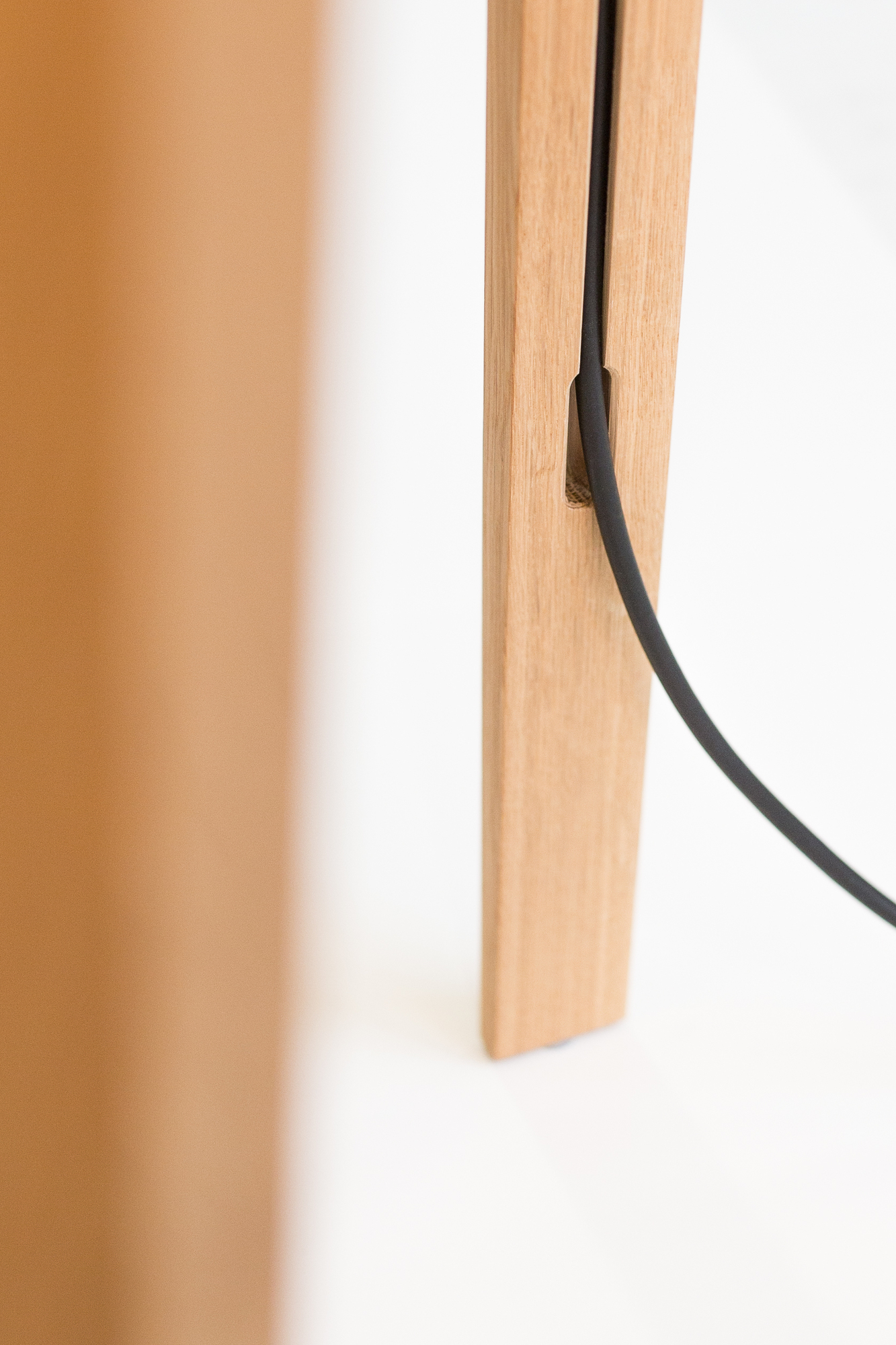Detailaufnahme der Luca Lean Anlehnleuchte von Maigrau: Holzfuß mit schwarzem Kabel, minimalistisches Design für Wohnraumbeleuchtung.