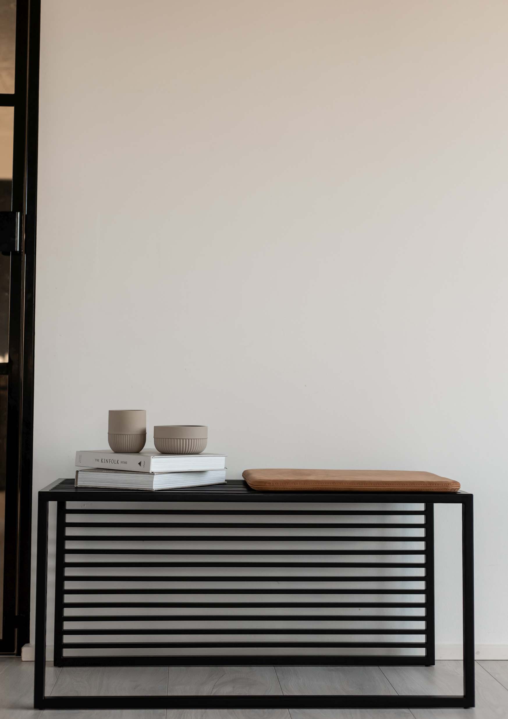 Element Bench Bank novoform mit schwarzem Metallgestell, braunem Sitzkissen, Büchern und Keramikschalen vor einer weißen Wand.