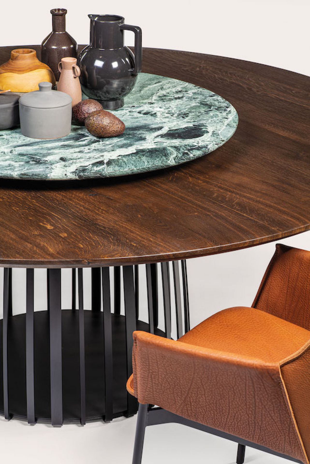 Detailaufnahme eines runden Esstisches aus dunklem Holz mit Marmorplatte und braunem Lederstuhl.