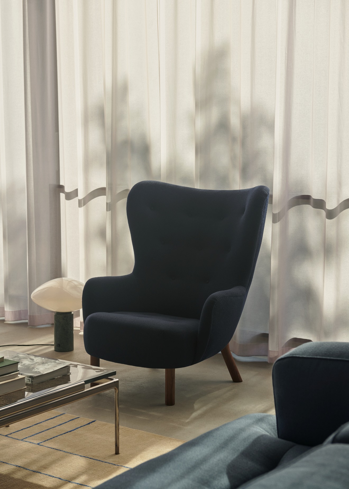 AndTradition Cruise Teppich AP23 in Beige mit blauem Muster unter Couchtisch und Sessel.