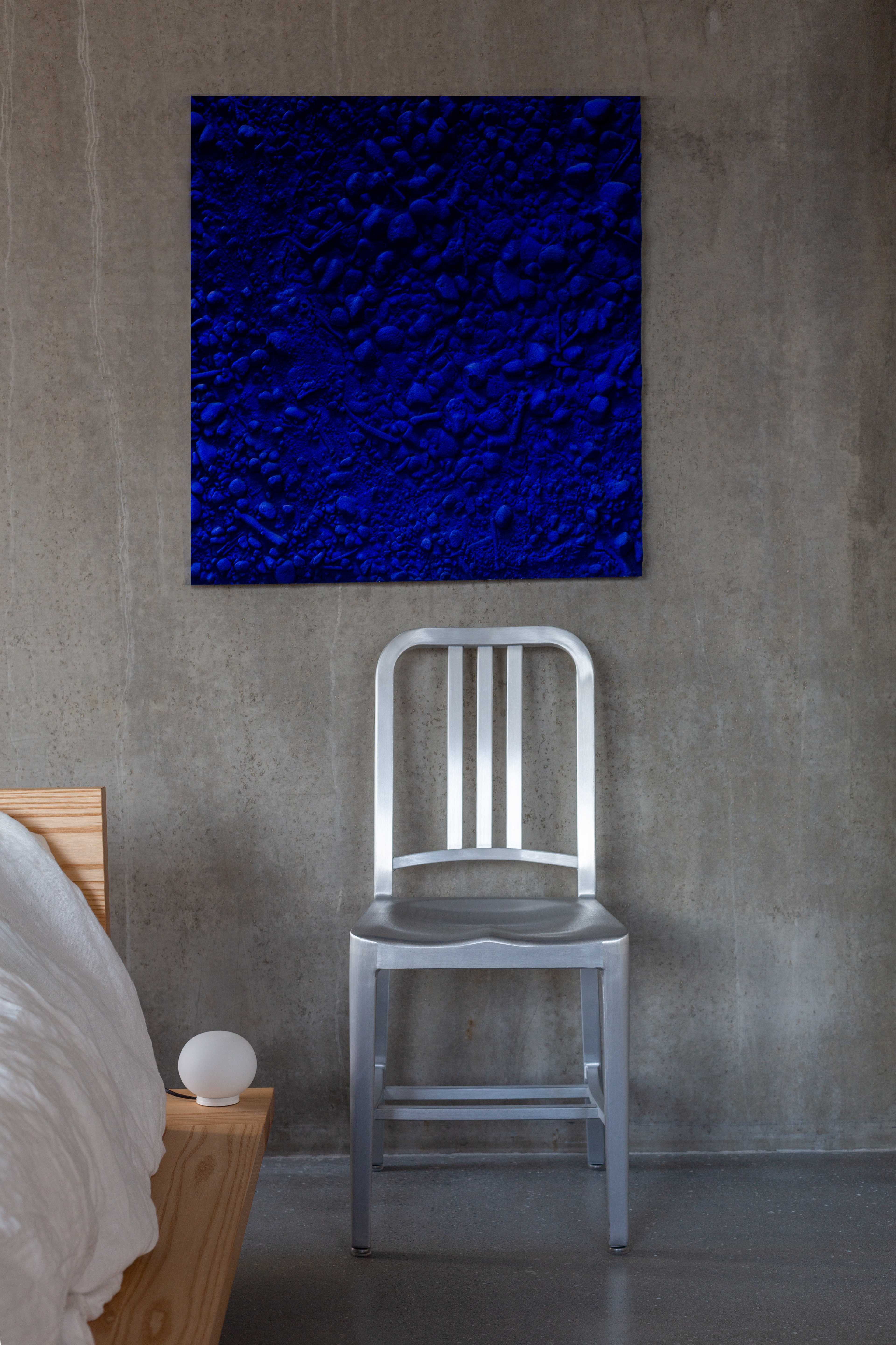 Classic Navy Chair von Emeco aus poliertem Aluminium vor einer Betonwand mit Kunstwerk.
