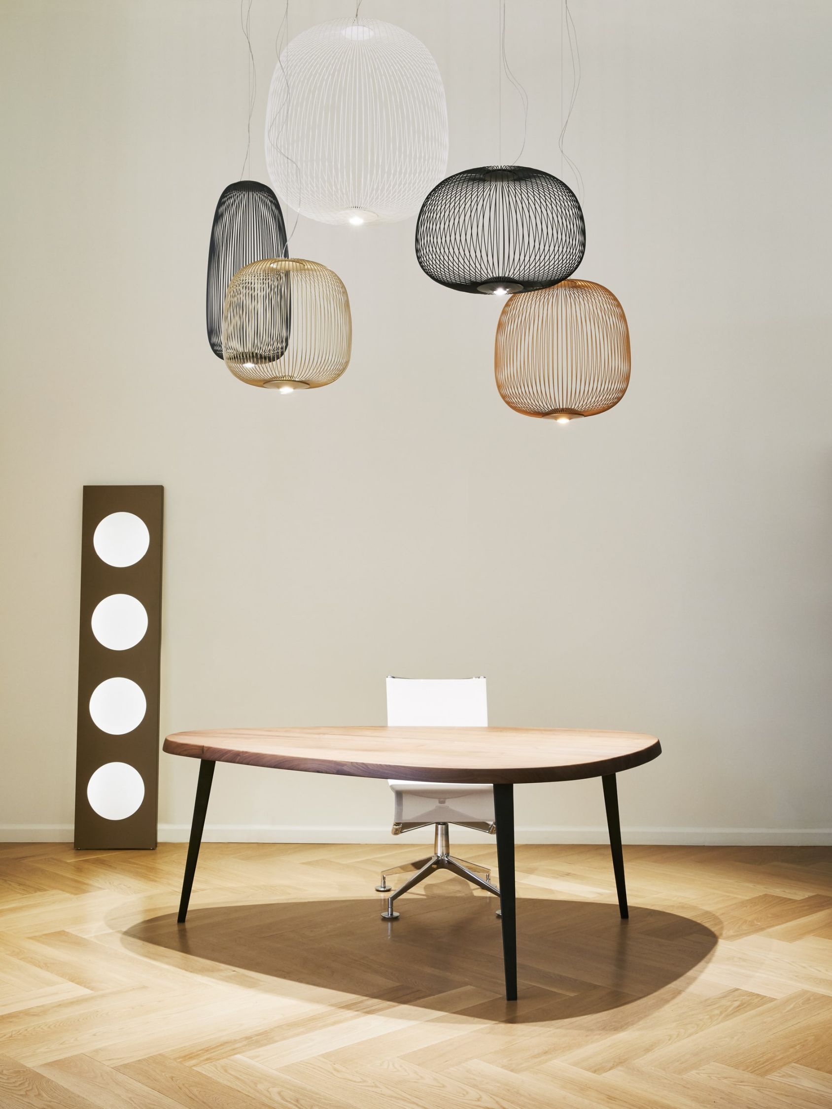 Mehrere Spokes Pendelleuchten von Foscarini, darunter eine schwarze, hängen über einem Holztisch.