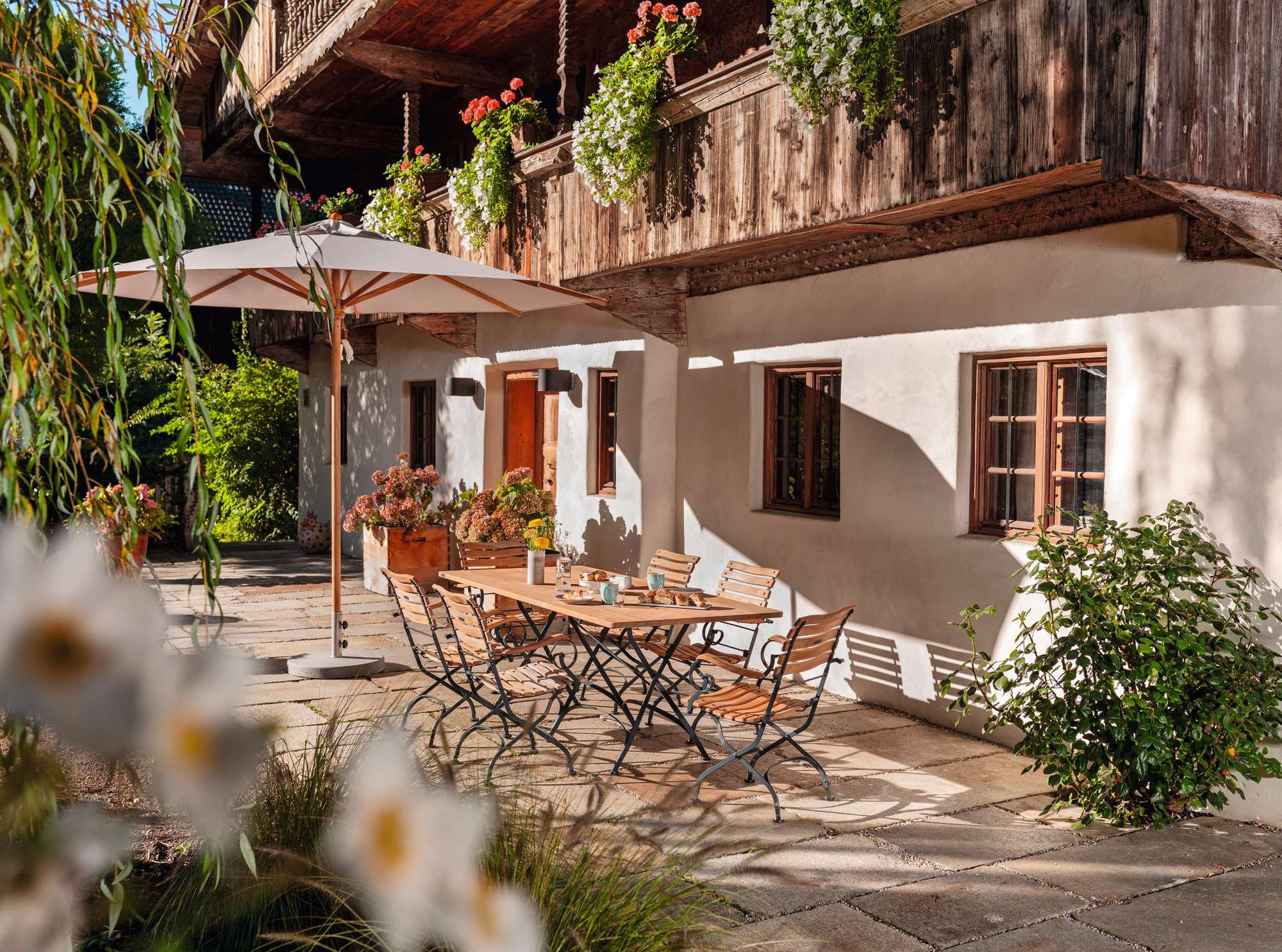 Gartenszene mit Weishäupl Classic Chair Stühlen und Tisch aus Holz im Außenbereich.