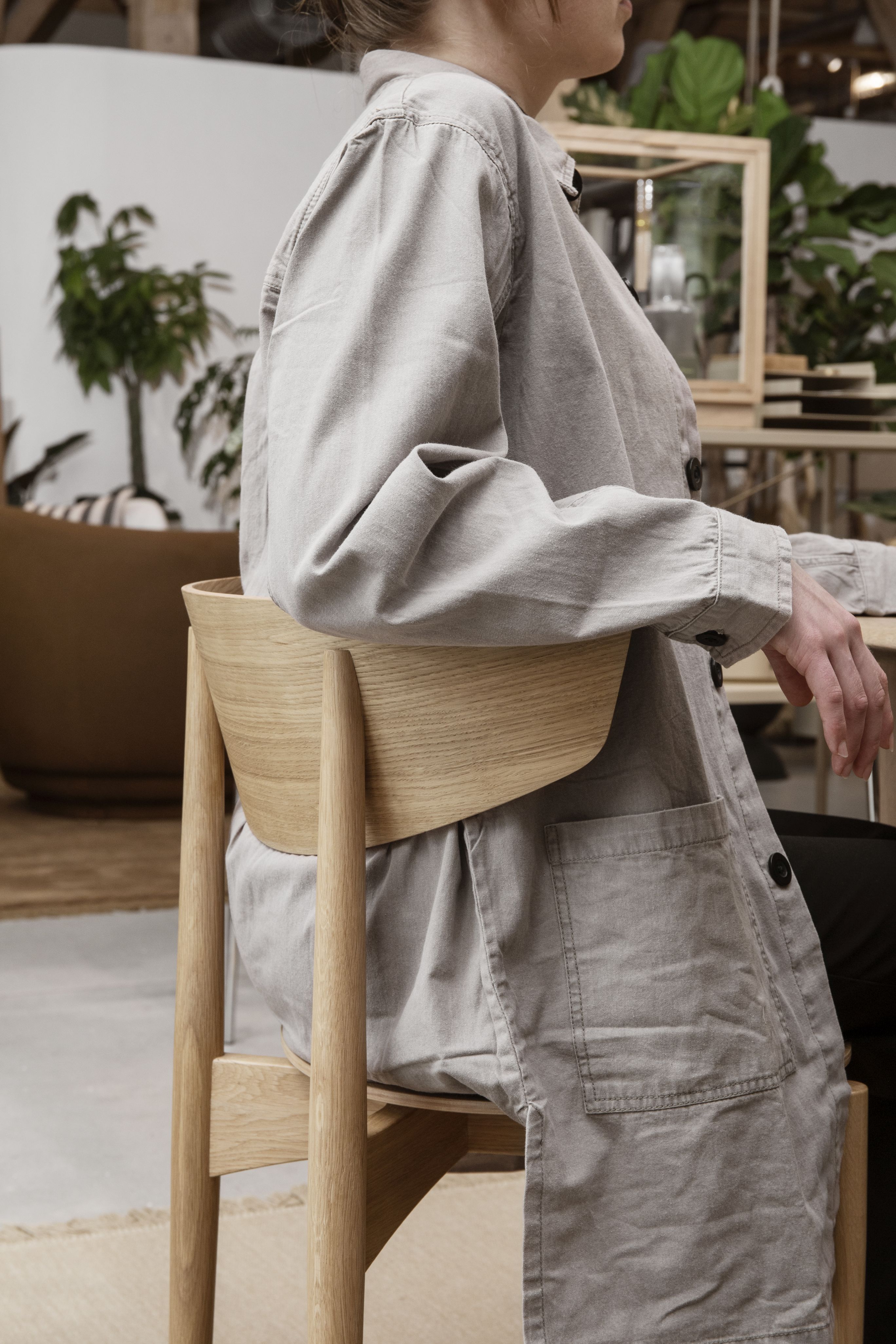 Frau sitzt auf einem Herman Stuhl von Ferm Living mit hellem Holzgestell.
