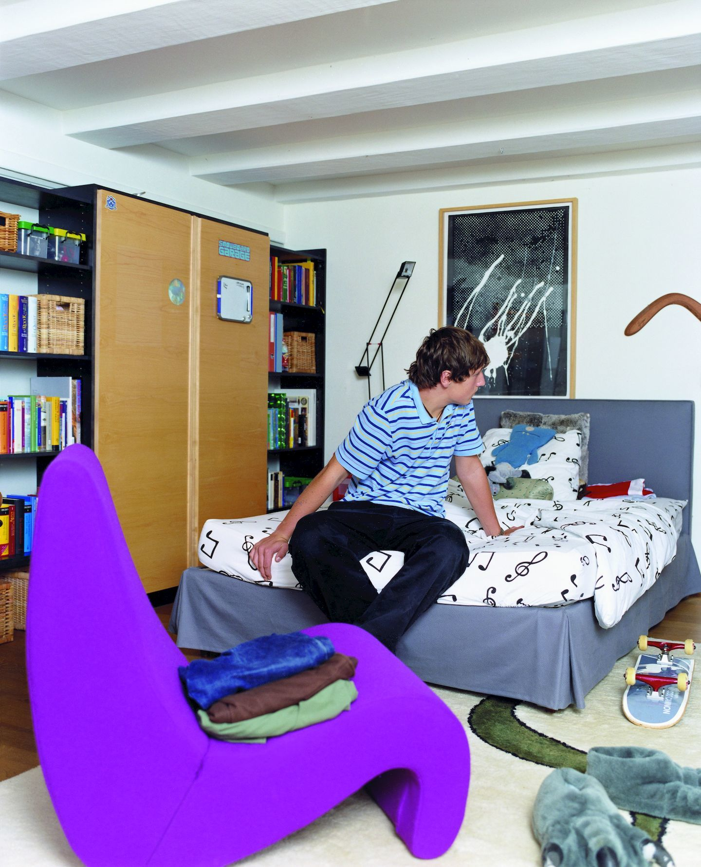 Lila Vitra Amoebe Sessel im Jugendzimmer mit Junge auf dem Bett und Bücherregal im Hintergrund.