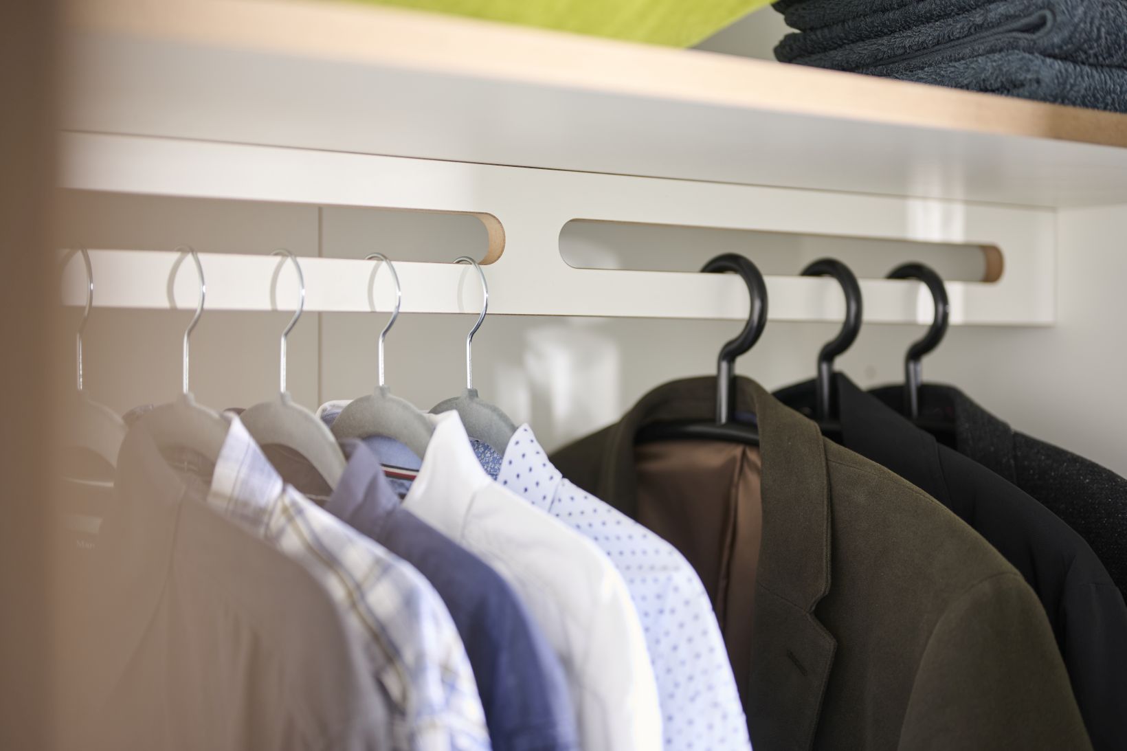 Innenansicht Tojo Schrank Grundmodul: Hemden und Jacken hängen ordentlich auf Kleiderbügeln im Schrank.
