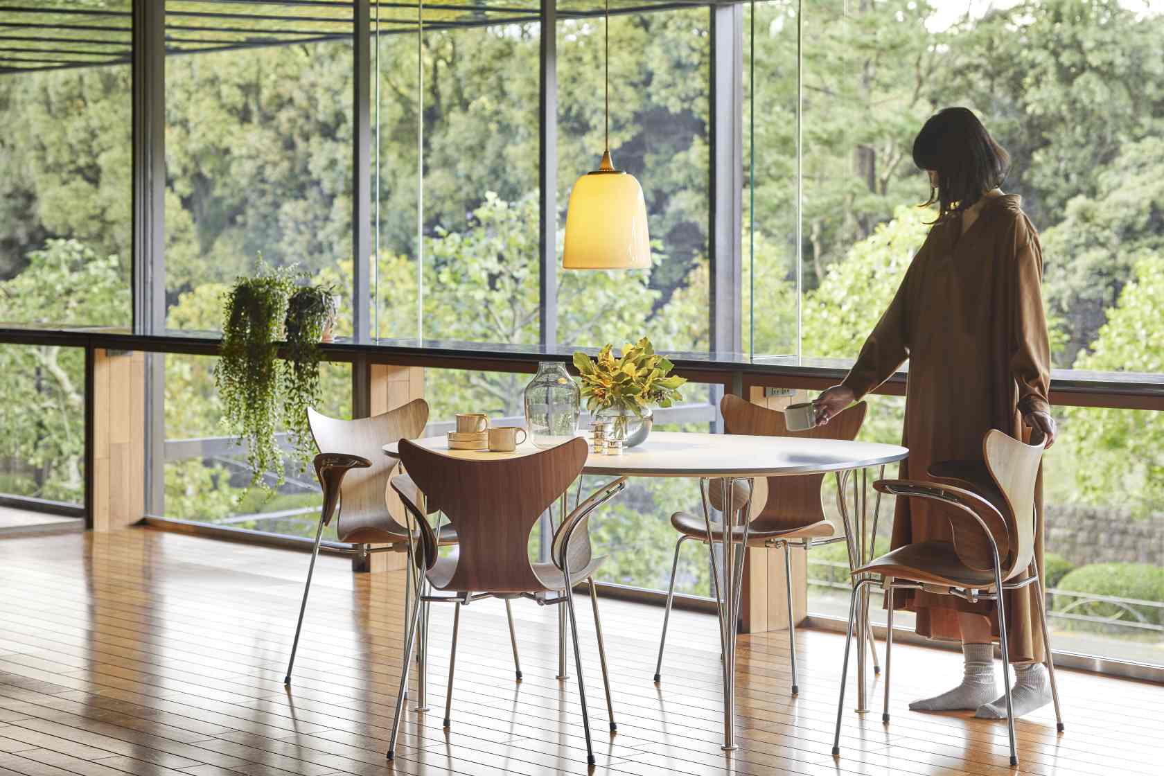 Fünf Fritz Hansen Lily Armlehnstühle aus Holz und Chrom um einen runden Esstisch in modernem Ambiente.