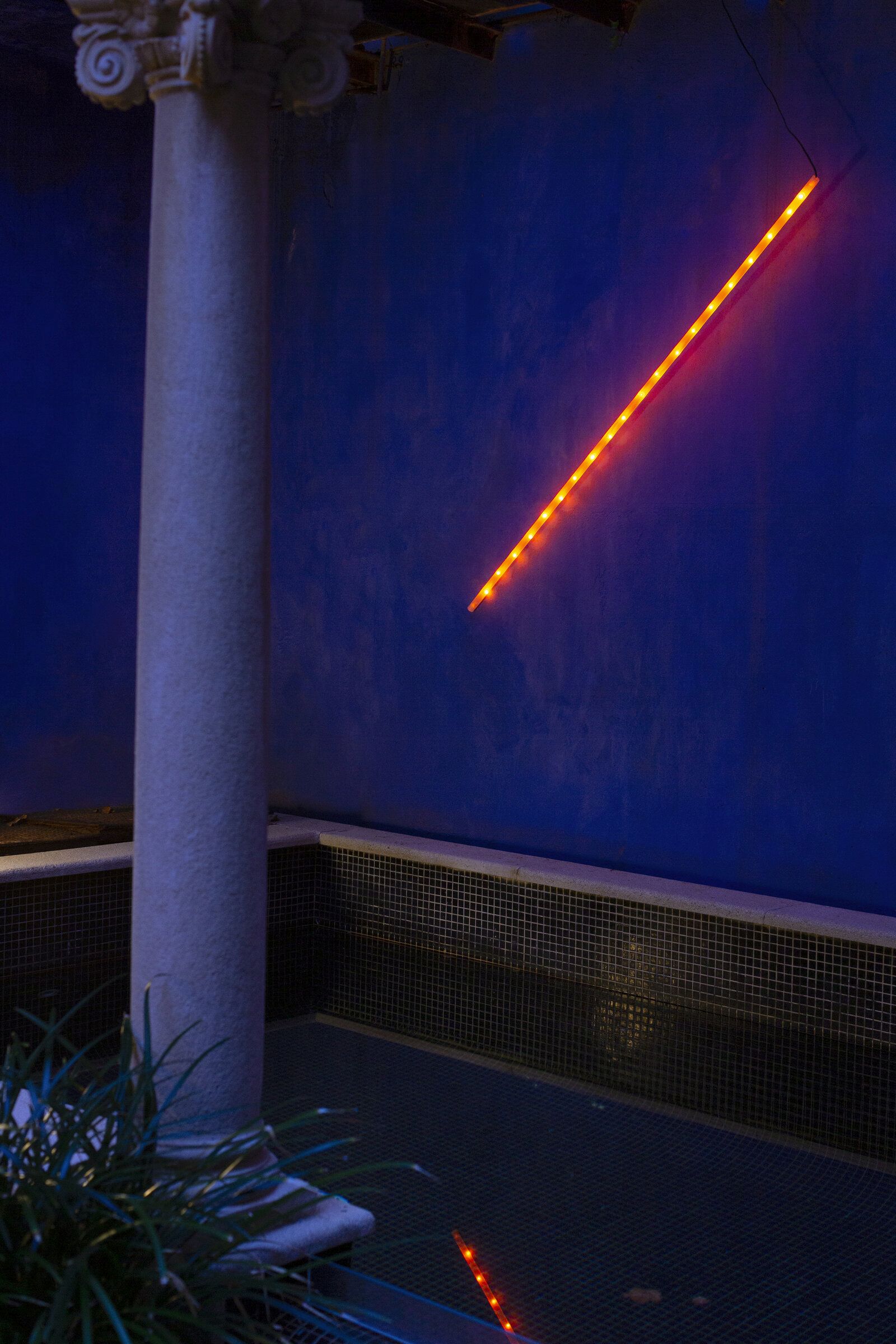 Orange LED-Leuchte an blauer Wand neben Säule, moderne Innenraumbeleuchtung für stimmungsvolles Ambiente.