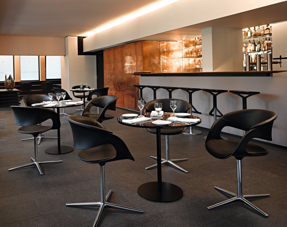 Innenaufnahme eines Restaurants mit mehreren Walter Knoll Lox Tischen und schwarzen Stühlen mit silbernen Füßen.