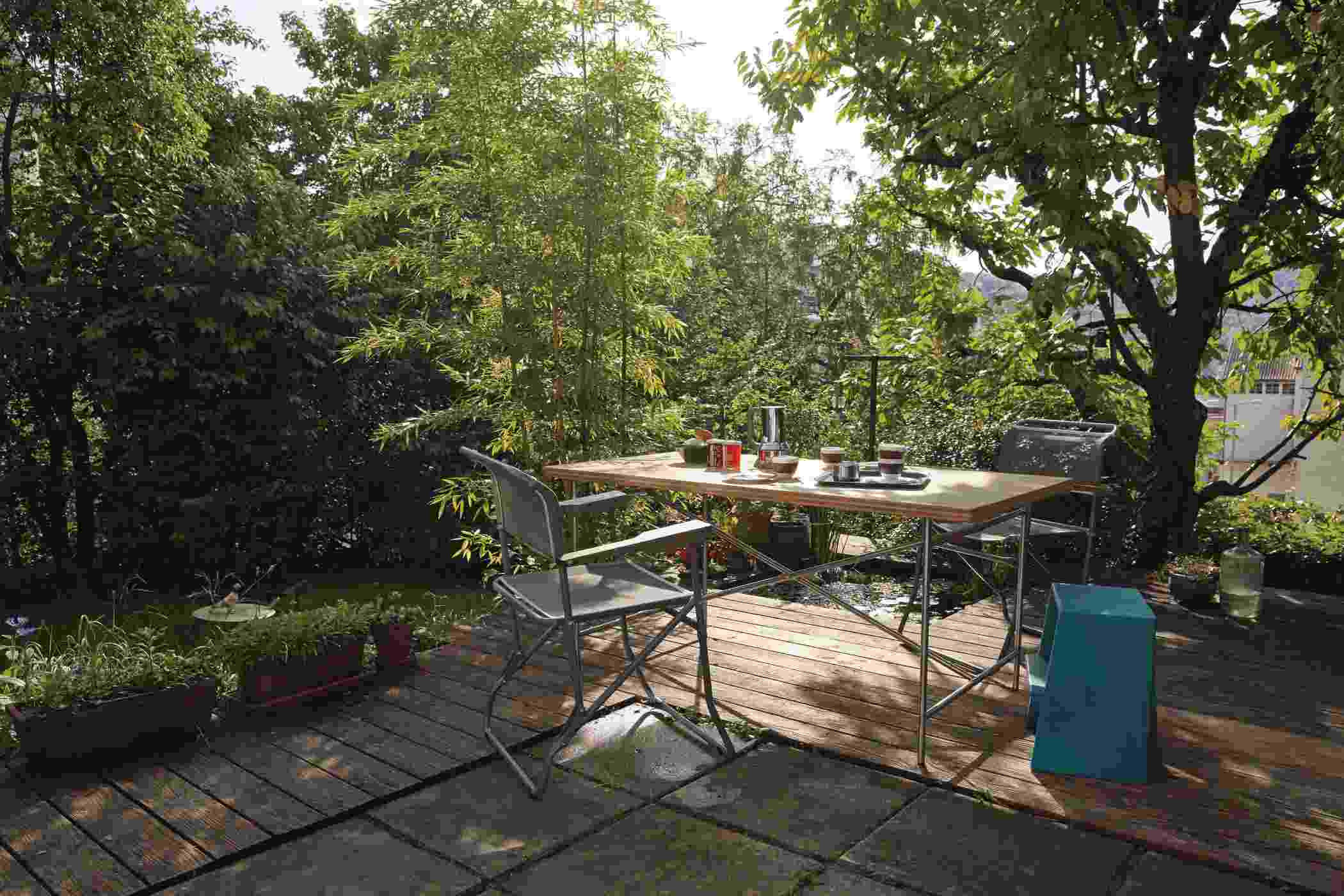 Eiermann Tisch mit Stahlgestell und zwei Stühlen auf einer Terrasse mit üppigem Grün.