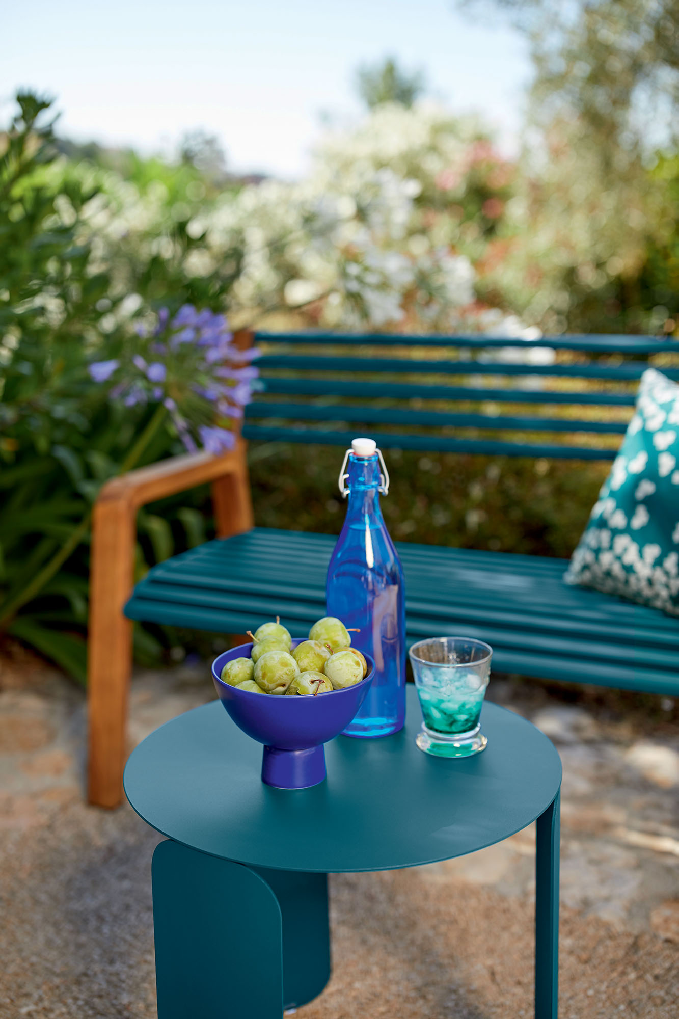 Somerset Bank Outdoor Fermob: Türkisblaue Gartenbank mit passendem Beistelltisch, Getränken und Obst.