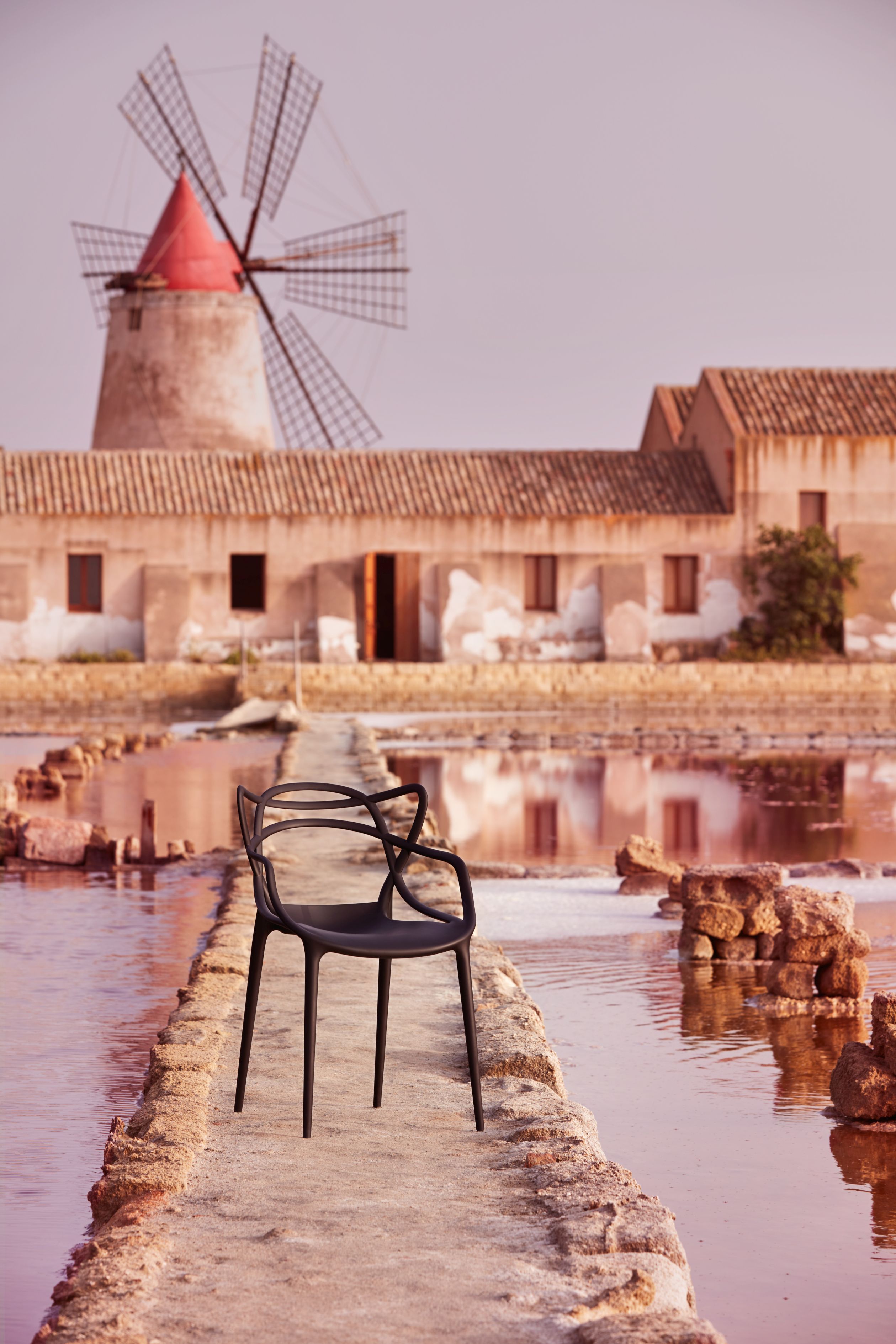 Schwarzer Masters Stuhl von Kartell im Freien, Design Stuhl mit Windmühle im Hintergrund.