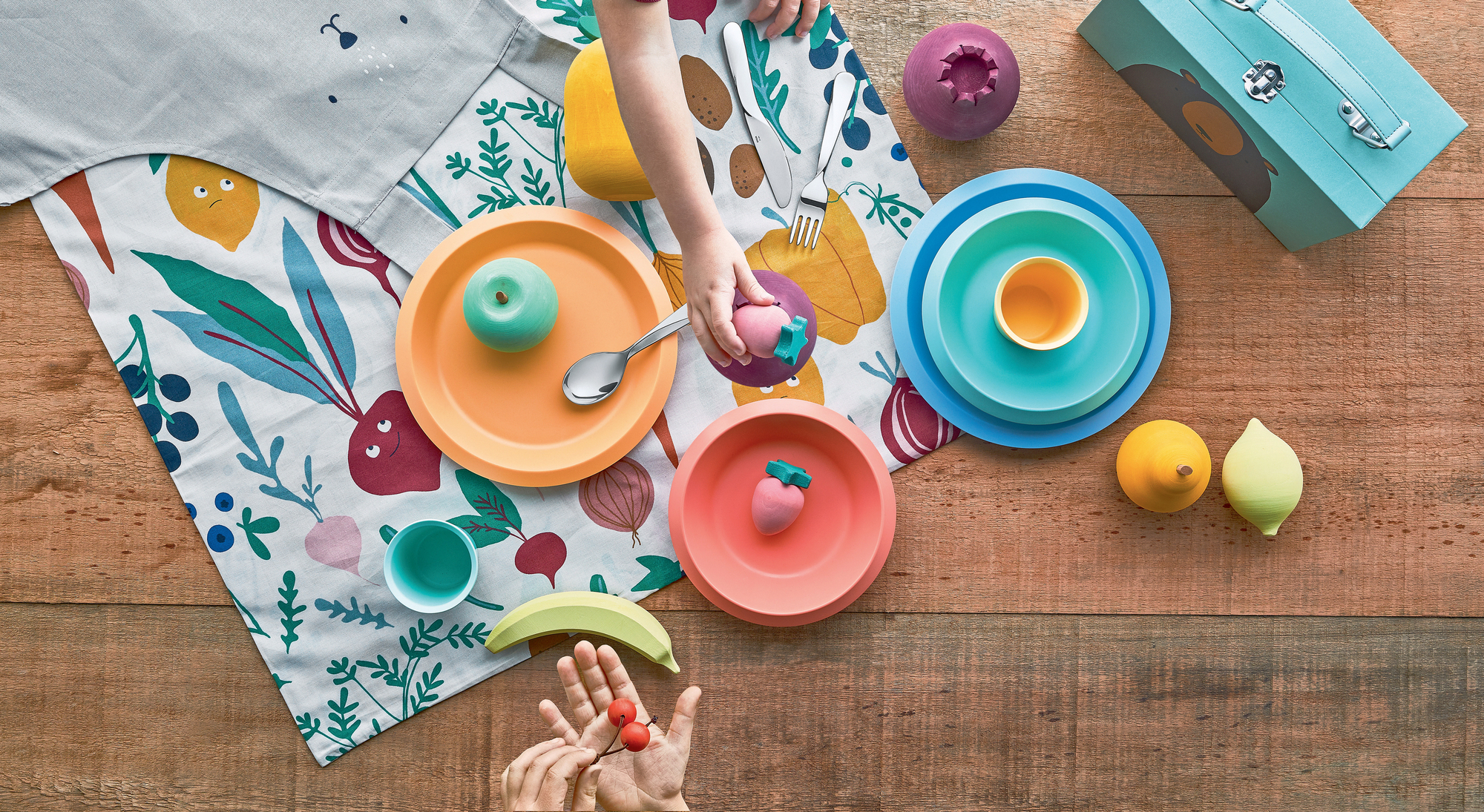 Giro Kids Collection Kinderbesteck aus Edelstahl mit bunten Tellern und Obstspielzeug auf Holztisch.