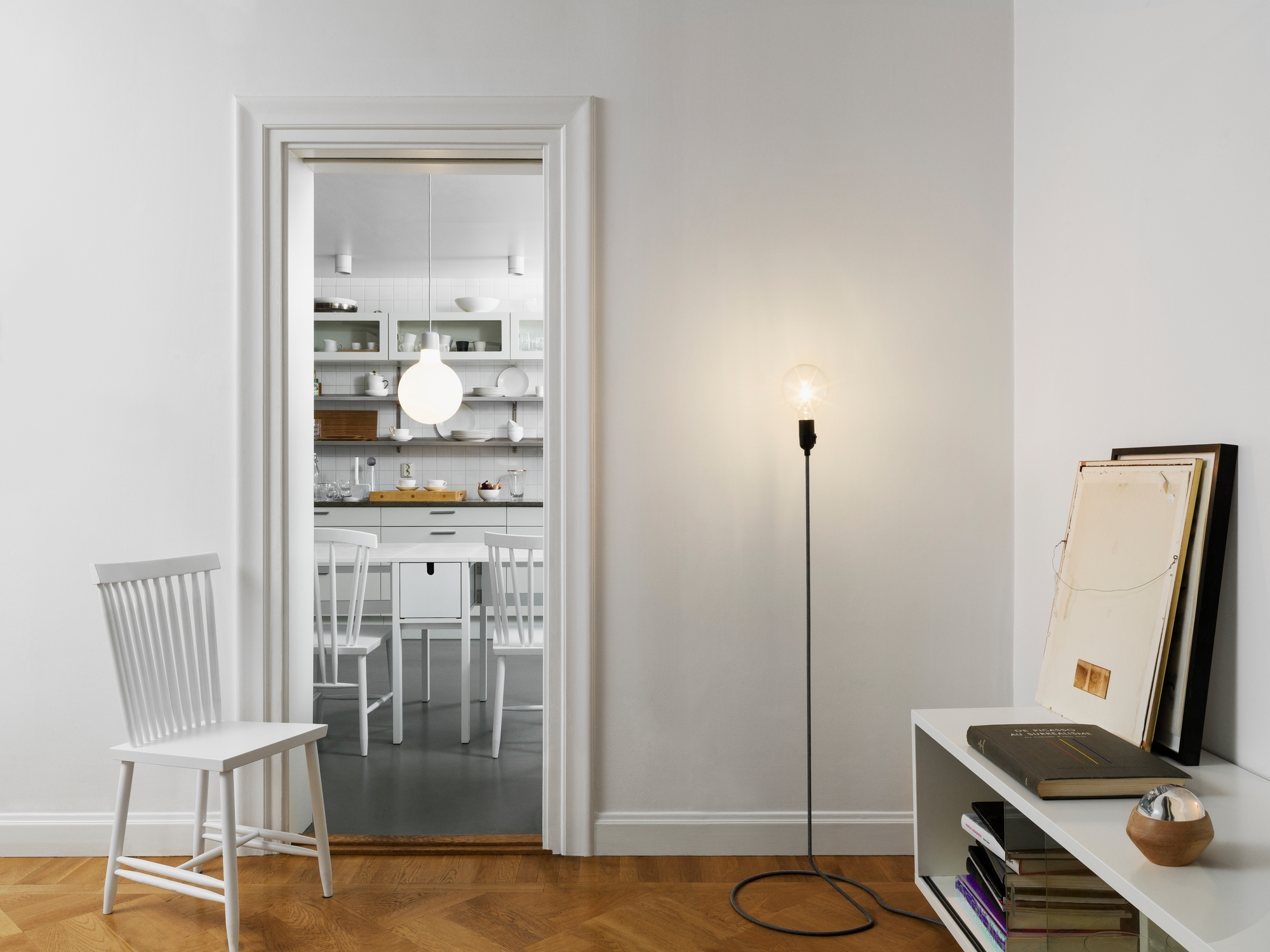 Helle Wohnung mit Design House Stockholm Cord Lamp Stehleuchte, Stuhl und Blick in die Küche.