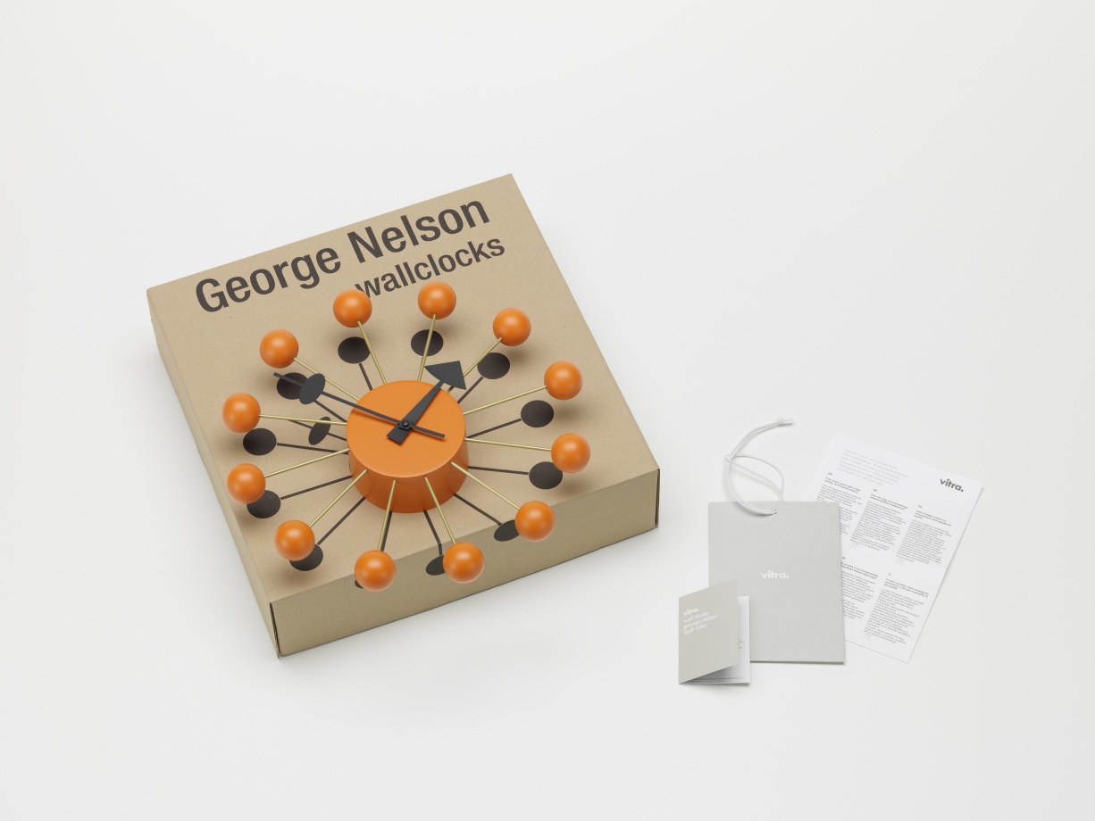 Orange Vitra Ball Clock Wanduhr auf Karton mit Anhänger und Broschüre, modernes Designobjekt für Wohnzimmer.