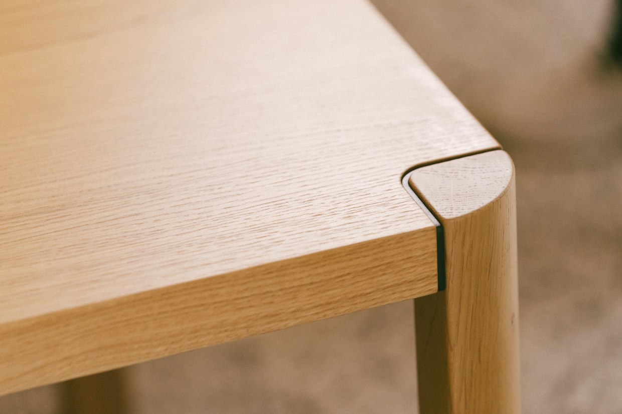 Detailaufnahme vom Thonet 1140 Esstisch: Tischplatte aus hellem Holz mit abgerundeter Ecke und Tischbein.