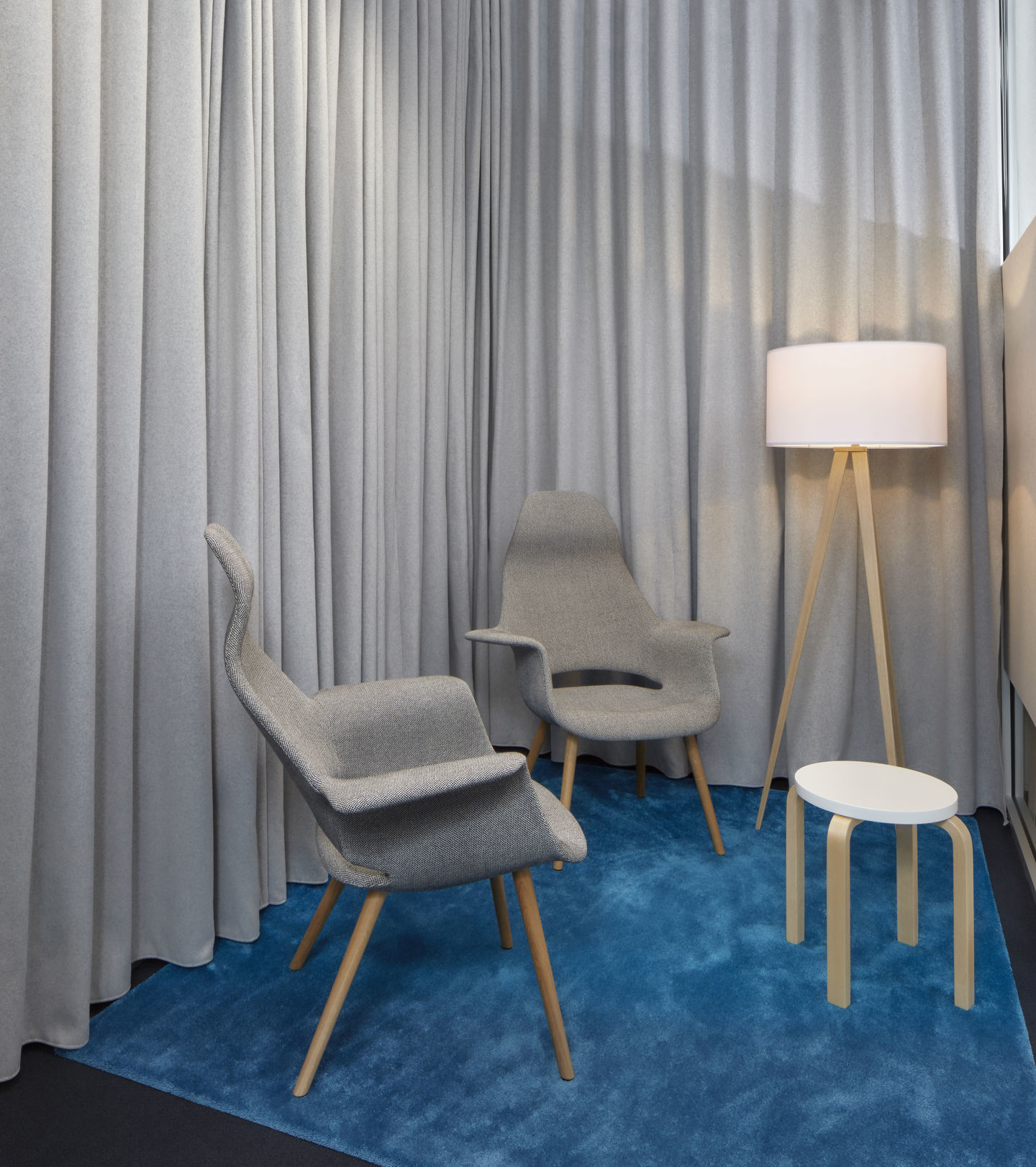 Zwei graue Organic Highback Stühle von Vitra mit Holzbeinen auf blauem Teppich, neben Stehlampe.
