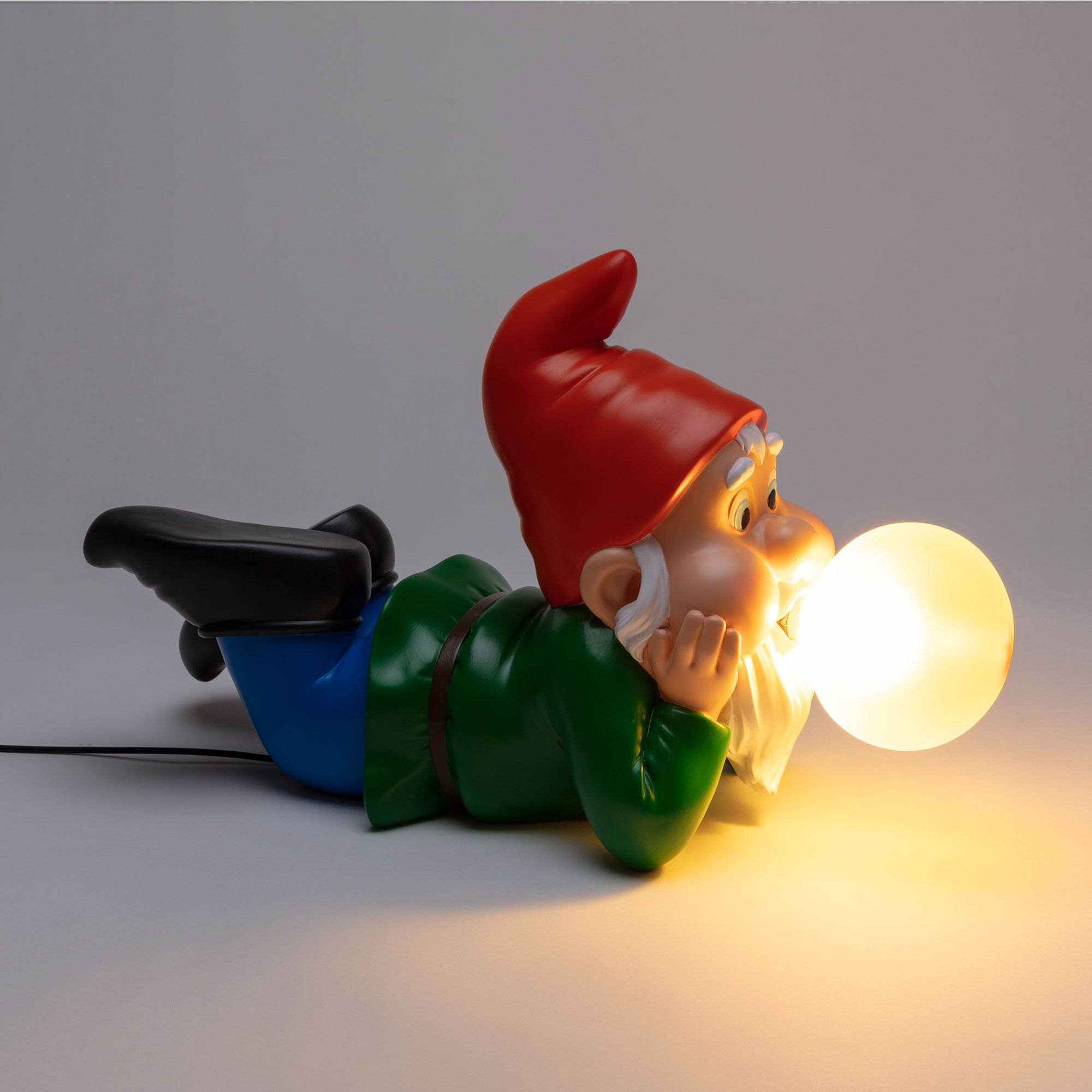 Gummy Dreaming Lampe von Seletti: Liegender Gartenzwerg mit roter Mütze und leuchtender Glühbirne im Mund.