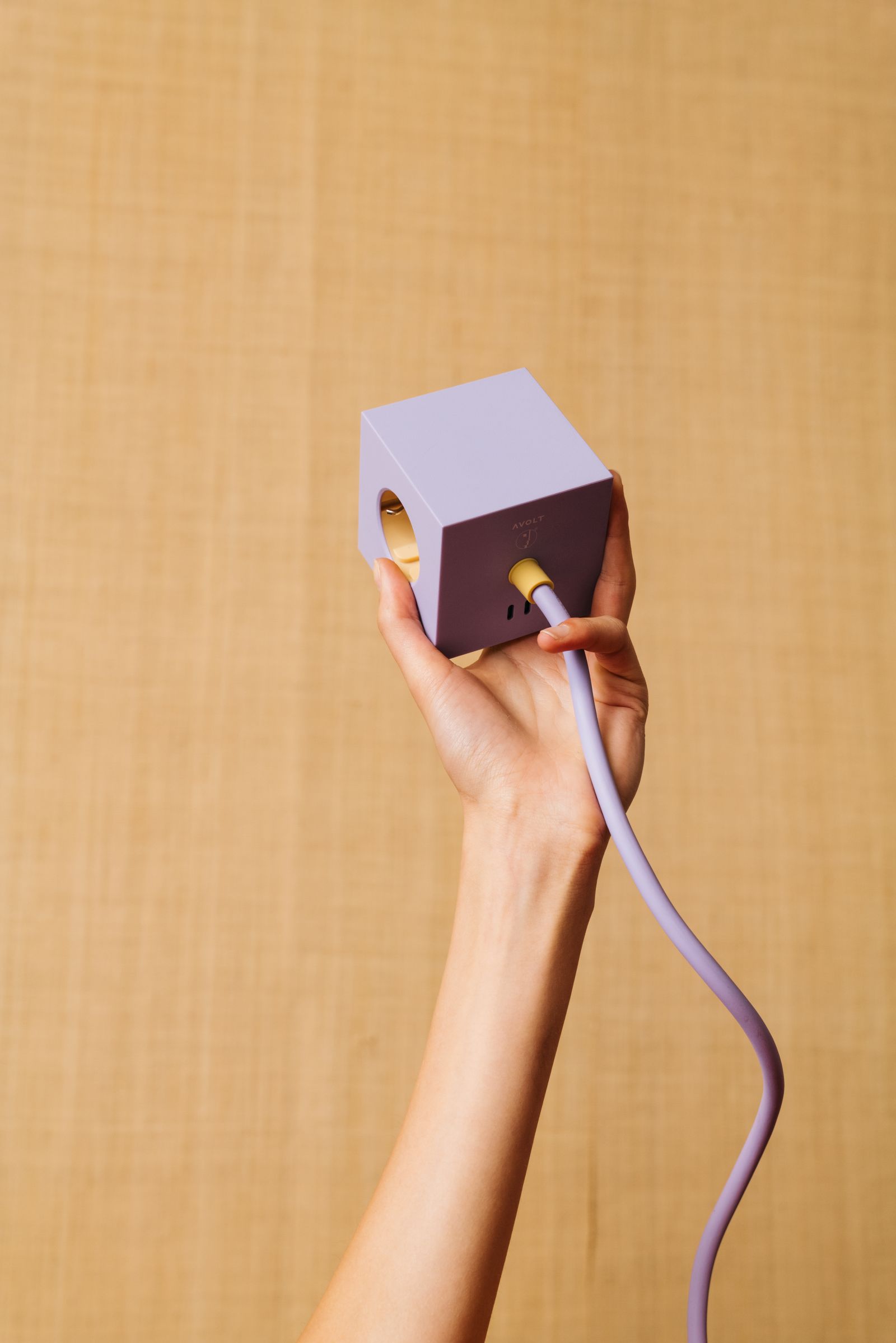Hand hält Avolt Square 1 Steckdosenwürfel in Lila mit USB-C Anschluss und Kabel.