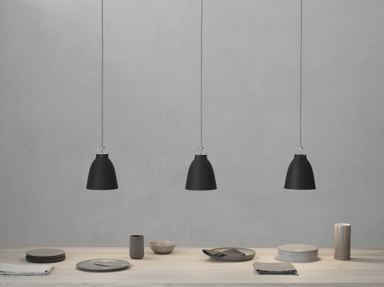 Drei schwarze Caravaggio Pendelleuchten von Fritz Hansen hängen über einem gedeckten Esstisch in minimalistischem Design.