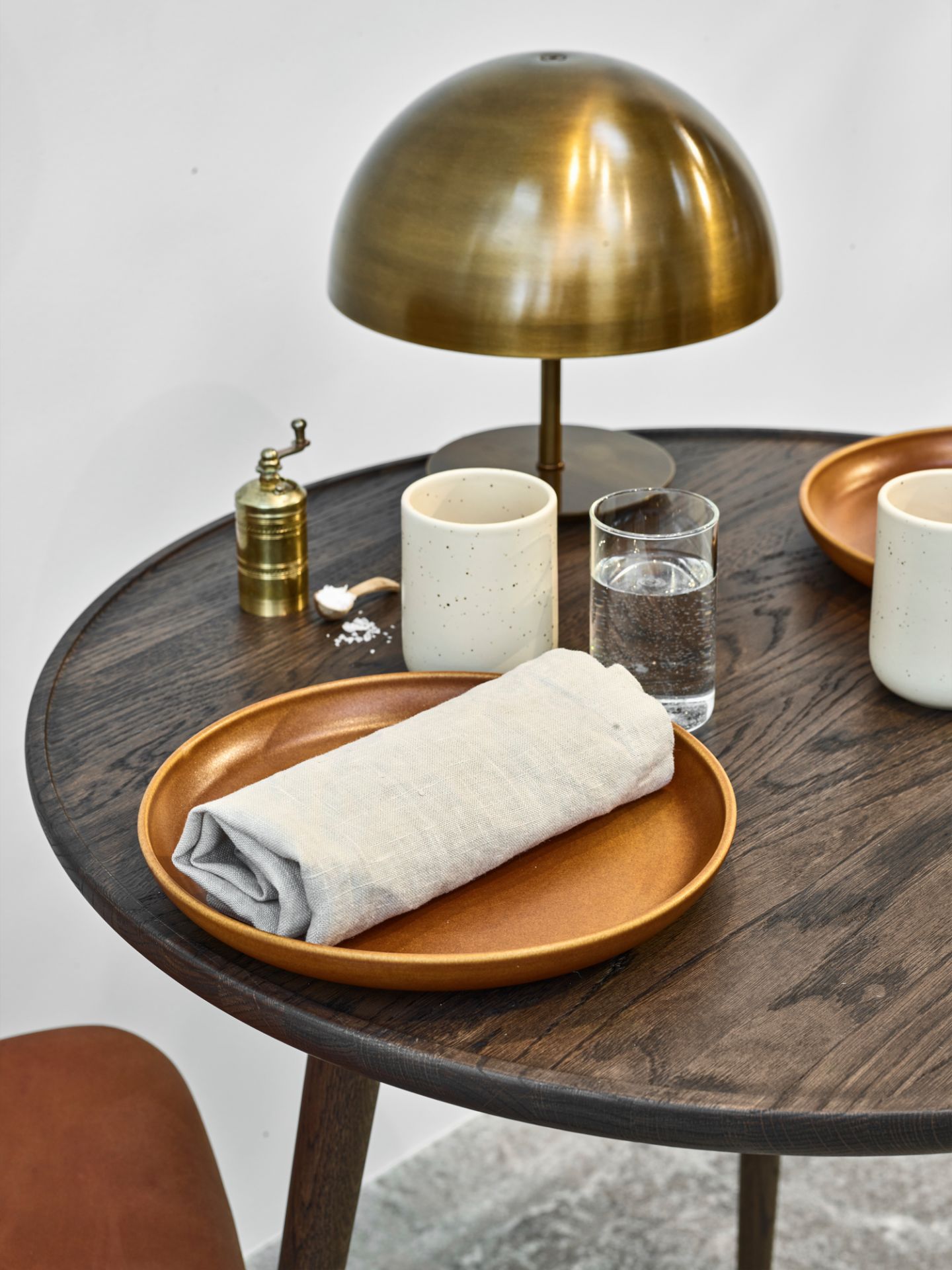 Nahaufnahme eines gedeckten Tisches mit Geschirr, Leinentuch, Lampe und Getränken auf dunklem Holz.
