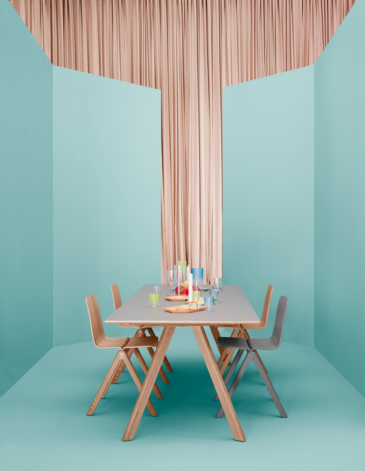 Heller Copenhague Table CPH 30 Esstisch aus Holz mit Stühlen und Tischdeko vor farbigem Hintergrund.