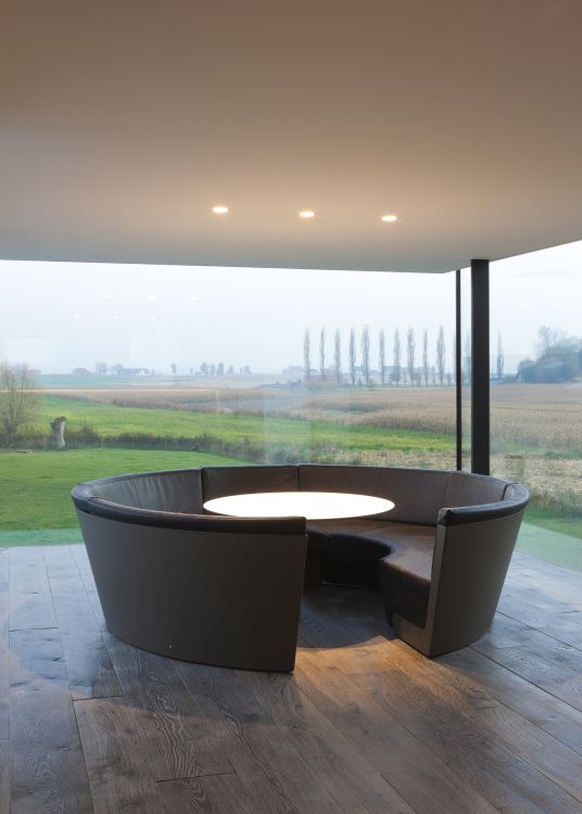 Runde Ledersitzgruppe mit weißem Tisch in modernem Raum mit Panoramablick auf die Landschaft.