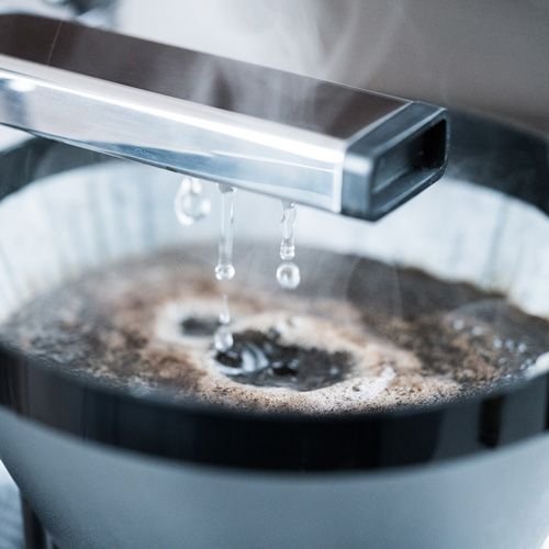 Detailaufnahme: Wasser tropft aus einer Kaffeemaschine in einen Filter mit Kaffeepulver. Pour-Over-Kaffeezubereitung.