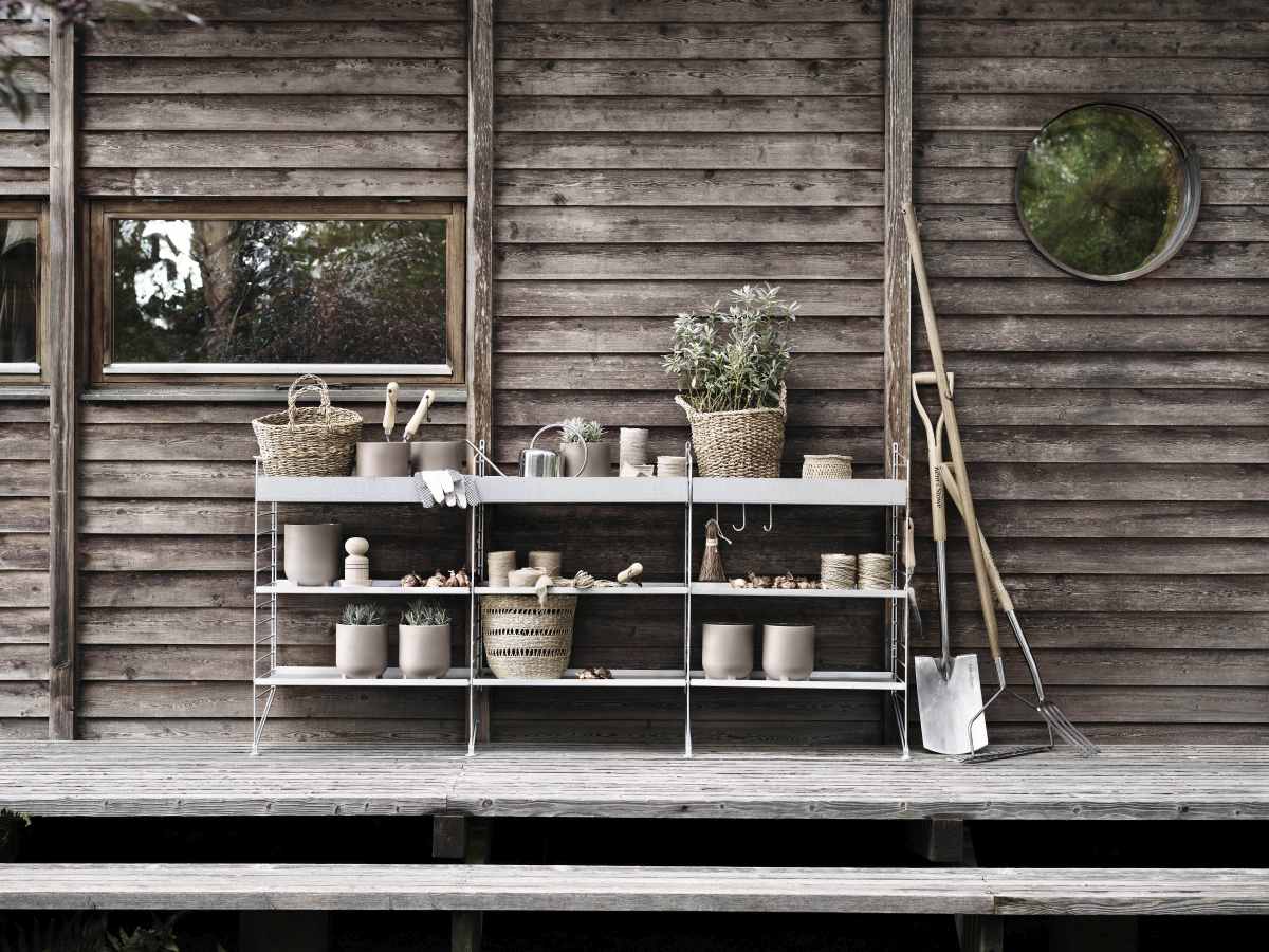 String Outdoor Regalsystem vor Holzwand mit Gartenzubehör, Bodenregal für Garten und Terrasse.