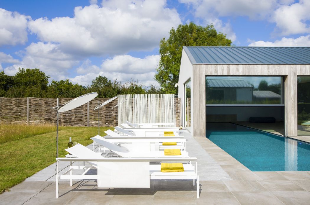 Weiße Extremis Sol + Luna Sonnenliegen am Pool mit Sonnenschirmen und gelben Handtüchern. Outdoor-Möbel für Garten und Terrasse.