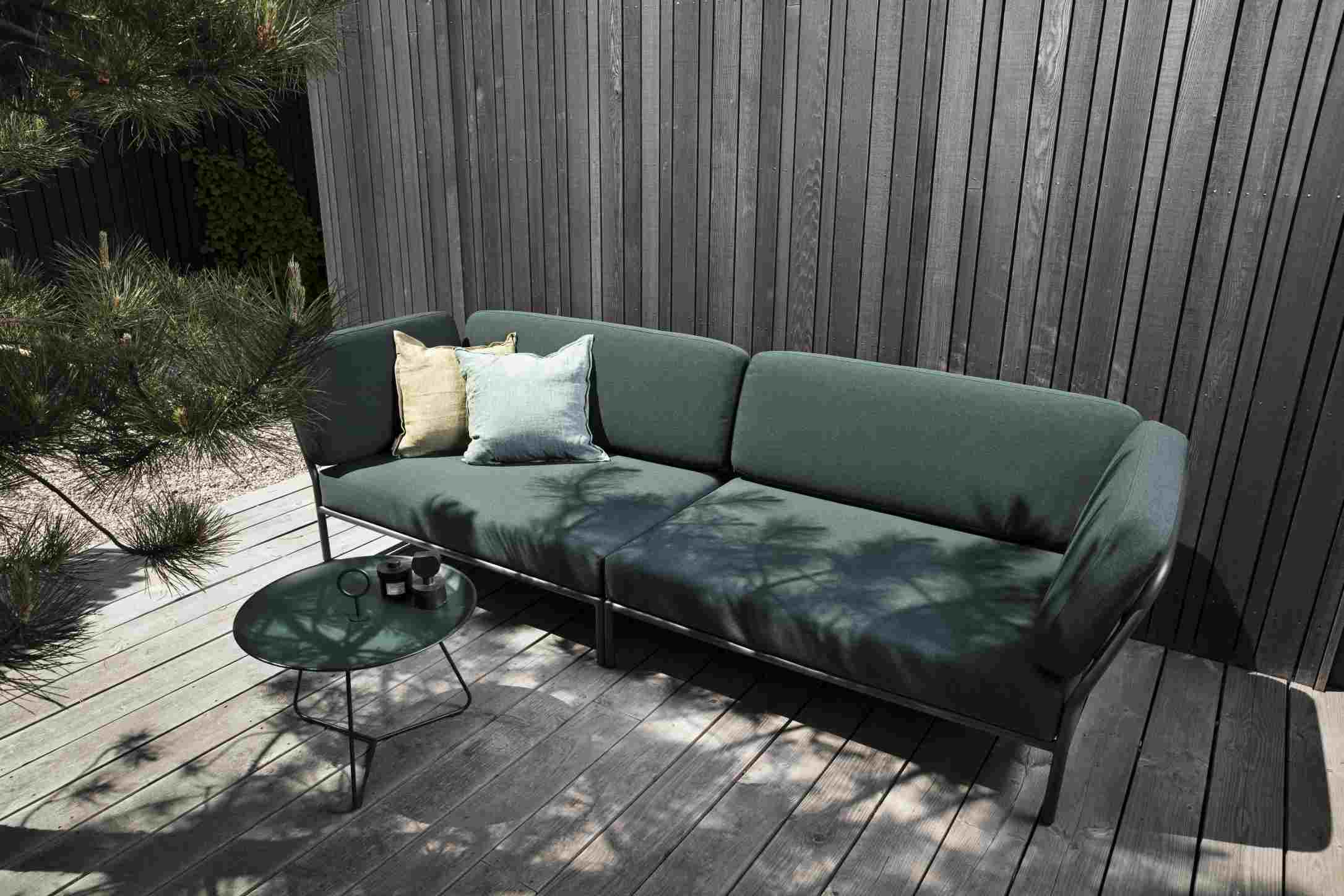 Houe Level Outdoor Sofa mit grüner Polsterung und Kissen auf einer Holzterrasse vor Holzwand.