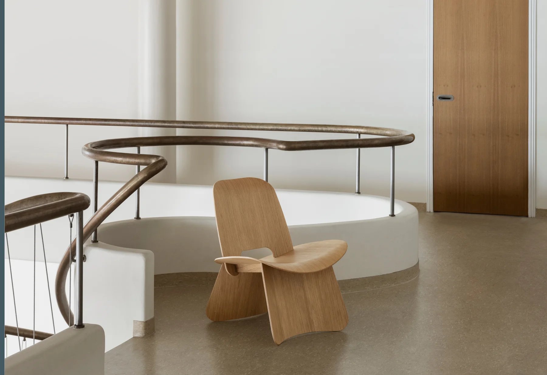 Blomus Nagomi Chair Stuhl aus hellem Holz vor weißer Wand und Treppengeländer.