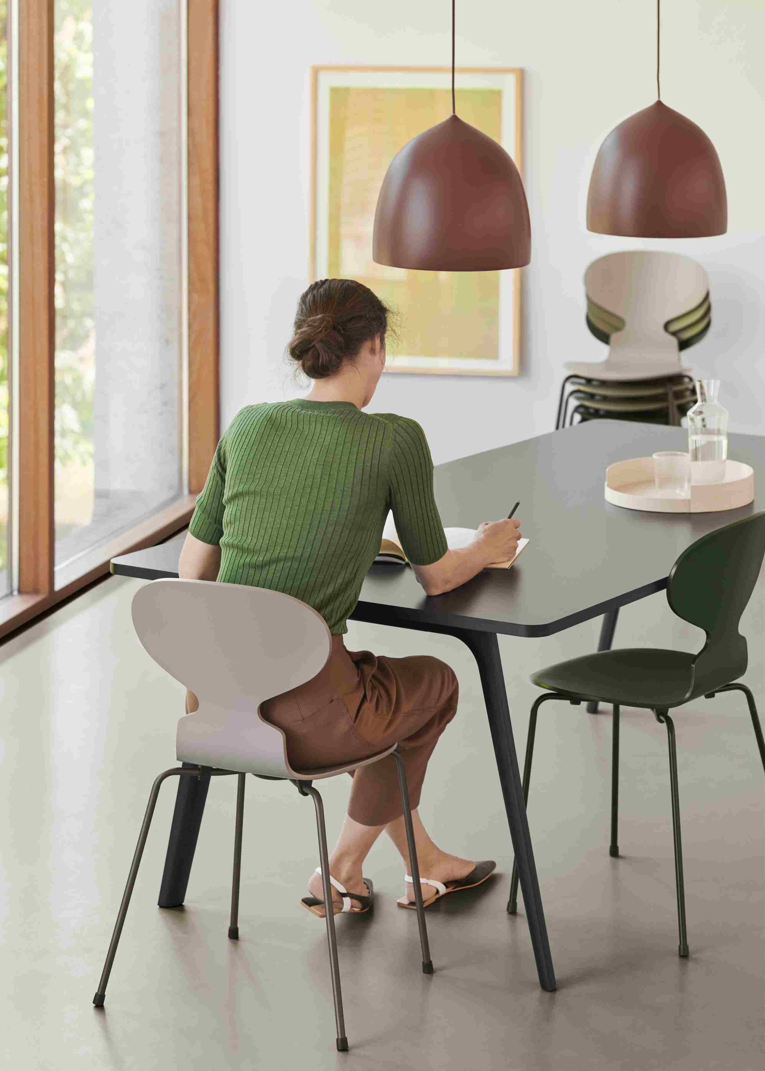 Frau sitzt am Tisch auf einem Fritz Hansen Ameise Stuhl mit vier Beinen in Beige.