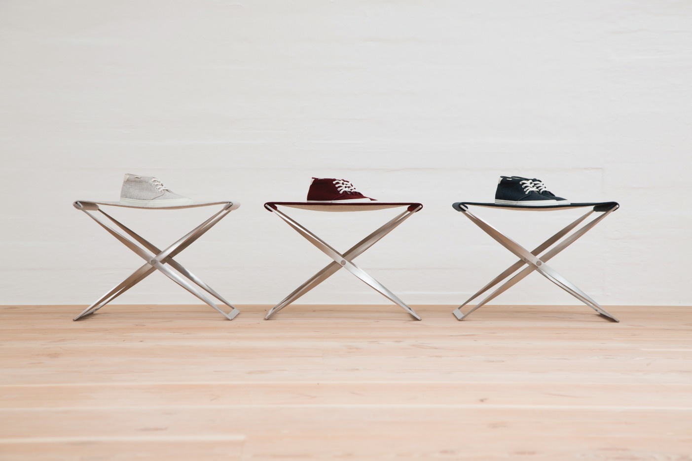 Drei PK91 Falthocker von Fritz Hansen in Grau, Rot und Blau mit Schuhen darauf.