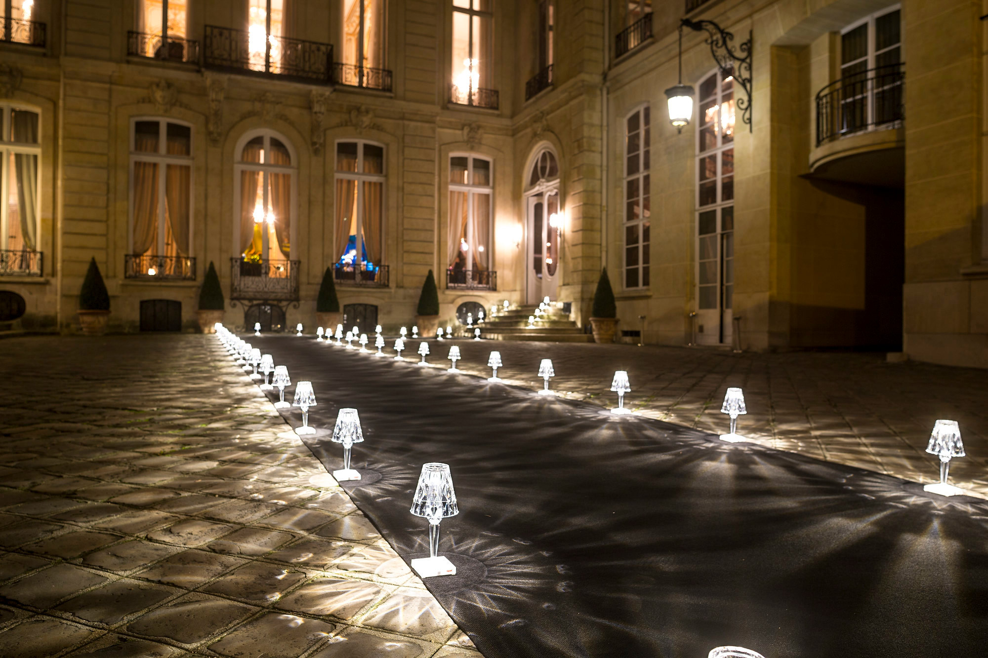 Reihe von Kartell Battery Tischleuchten in Rauch vor einem Gebäude bei Nacht.