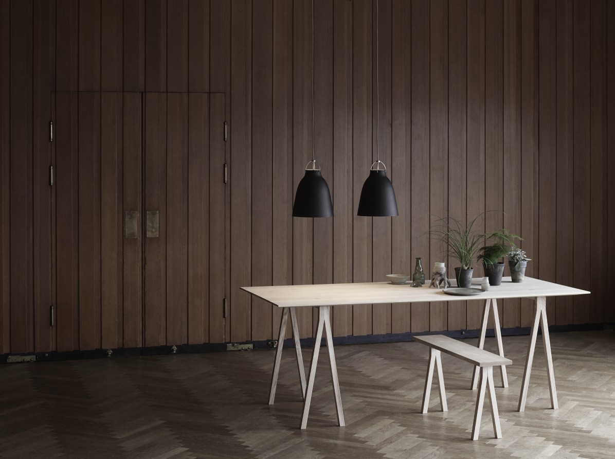 Zwei schwarze Caravaggio Pendelleuchten von Fritz Hansen über einem Esstisch mit Holzbank und Dekoration.
