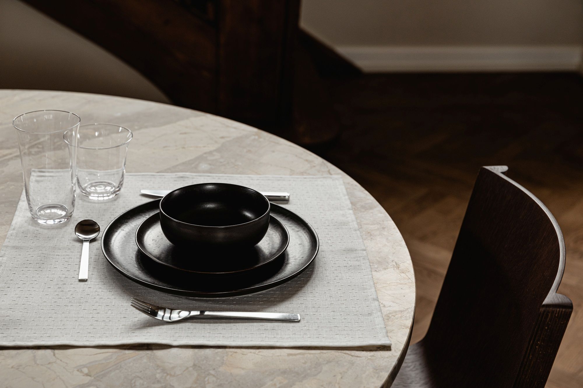 Detailaufnahme eines gedeckten Tisches mit Audo Copenhagen Ready Dining Chair Stuhl im Hintergrund, Fokus auf Geschirr und Besteck.