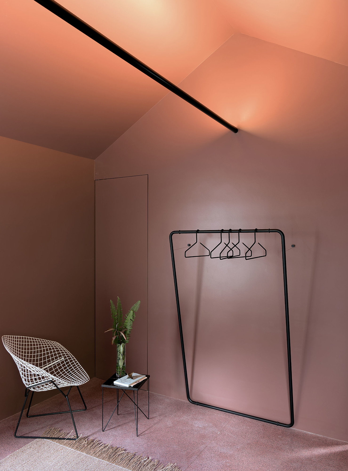 Schönbuch Curve Wandgarderobe in minimalistischem Raumdesign mit Stuhl, Beistelltisch und Kleiderbügeln vor rosa Wand.