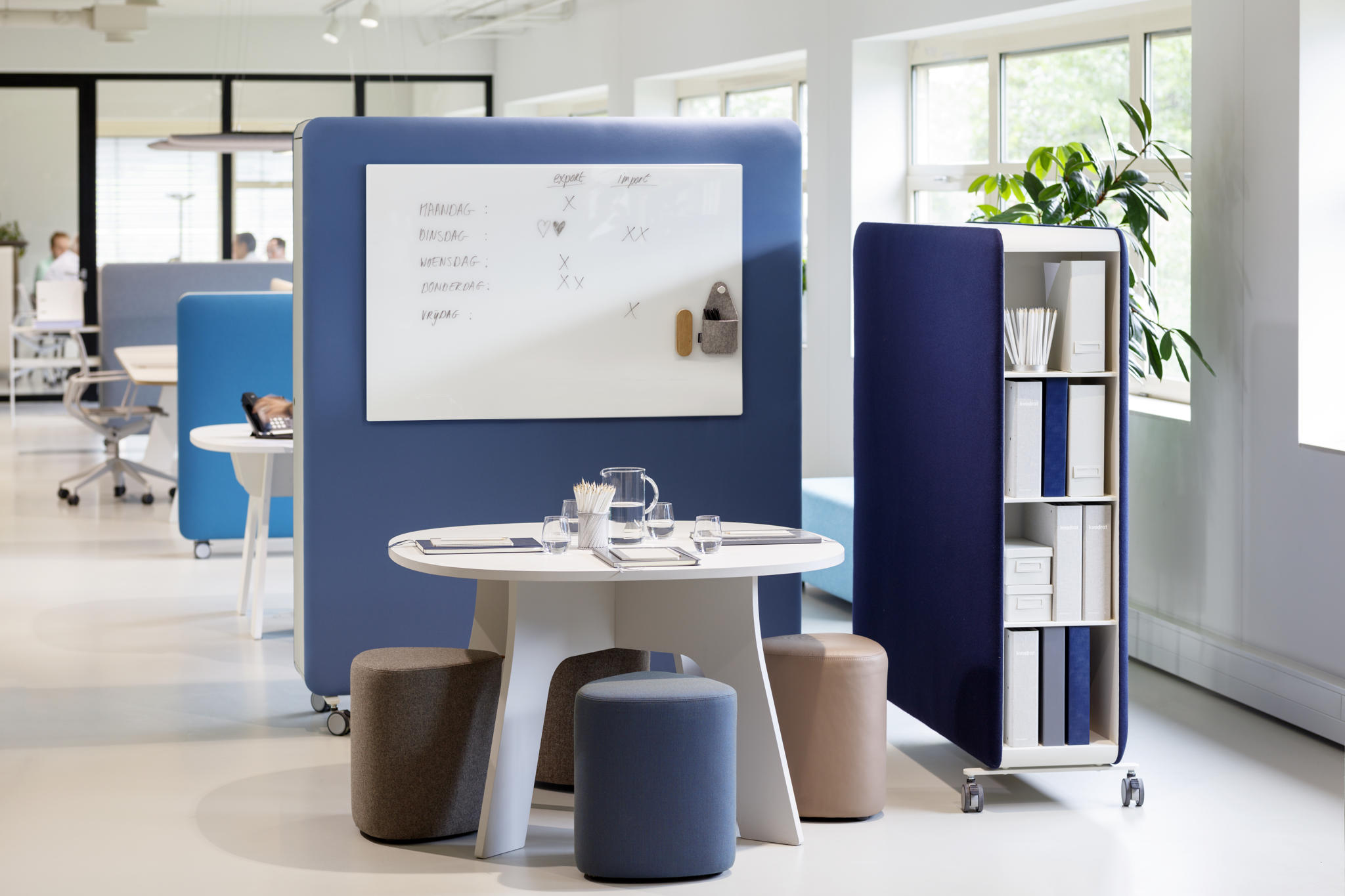 Büro mit Cascando Pillow Space Akustik-Raumteilern in Blau, Whiteboard, Tisch, Hocker und Regal.