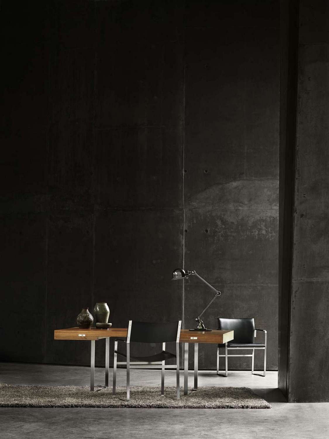 CH110 Tisch von Carl Hansen & Søn mit Stühlen und Lampe vor dunkler Betonwand.