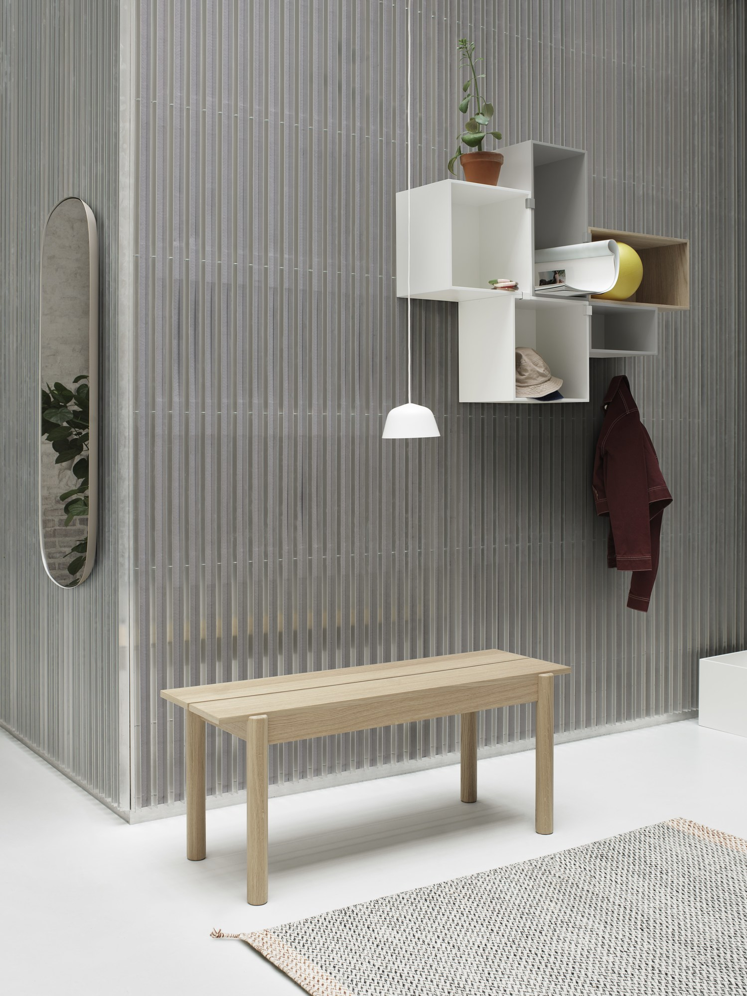 Helle Raumansicht mit weißer Ambit Pendelleuchte, Holzbank, Spiegel und Wandregal. Modernes Interior Design.