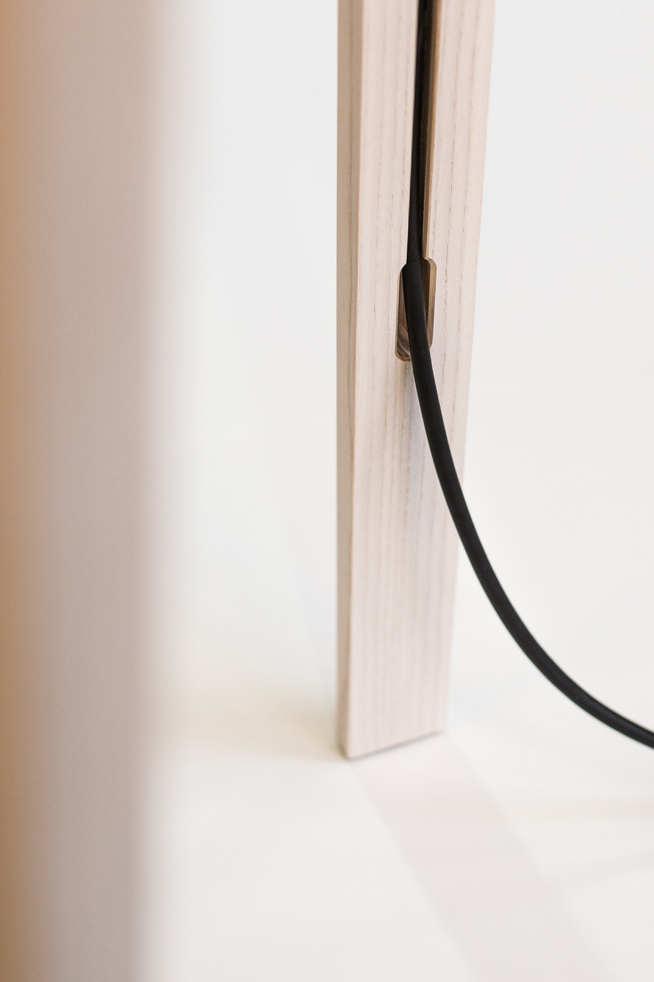 Detailaufnahme der Luca Lean Anlehnleuchte von Maigrau: Holzfuß mit schwarzem Kabel, minimalistisches Design für Wohnraumbeleuchtung.