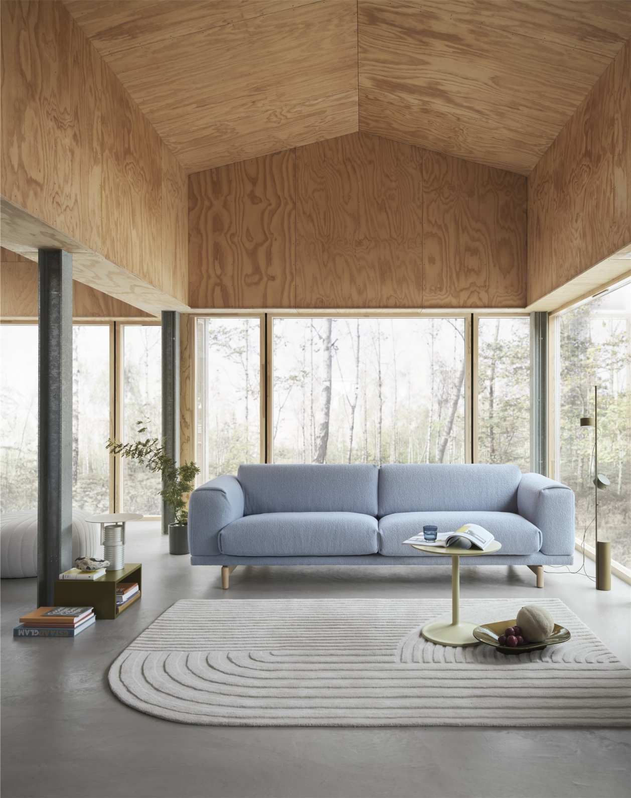Helle Wohnzimmer-Szene mit blauem Sofa, Teppich und einer Muuto Set Table Tischleuchte auf einem Beistelltisch.