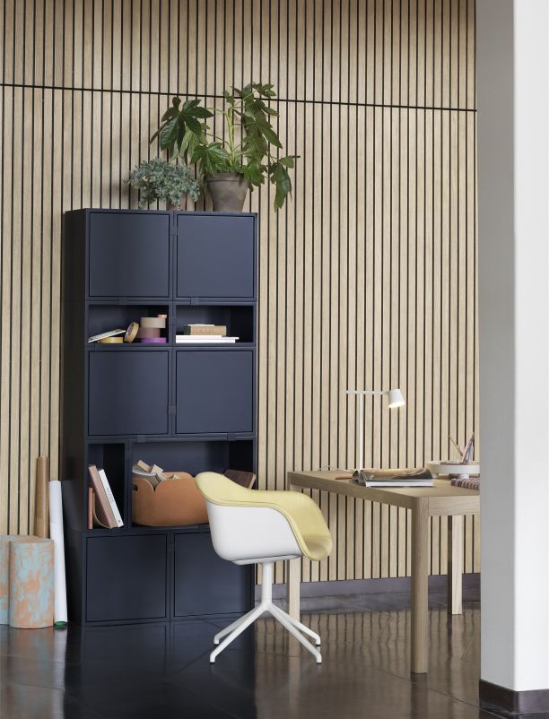 Modernes Büro mit blauem Regalsystem, Schreibtisch, gelbem Bürostuhl und Zimmerpflanzen vor Holzpaneelwand.