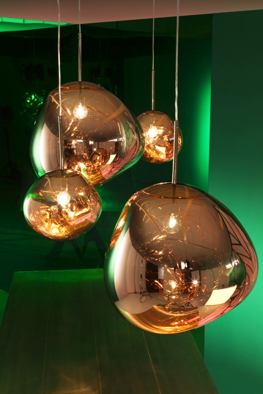 Nahaufnahme von vier goldenen Melt LED Hängeleuchten von Tom Dixon vor grünem Hintergrund.