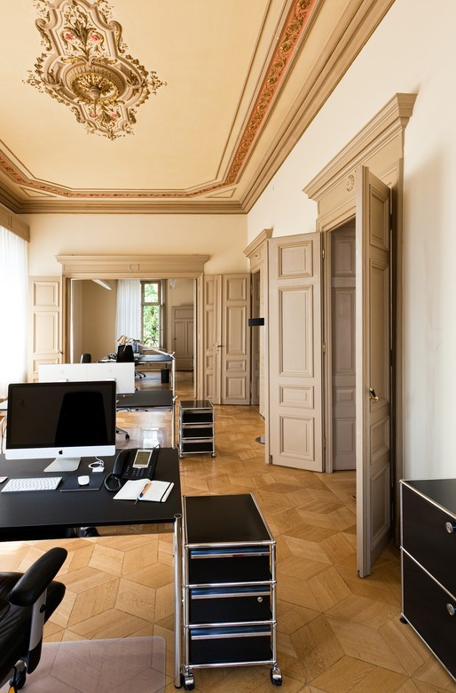 USM Haller Rollcontainer in Enzianblau im Büro mit Schreibtisch und Parkettboden. Moderner Büroschrank auf Rollen.